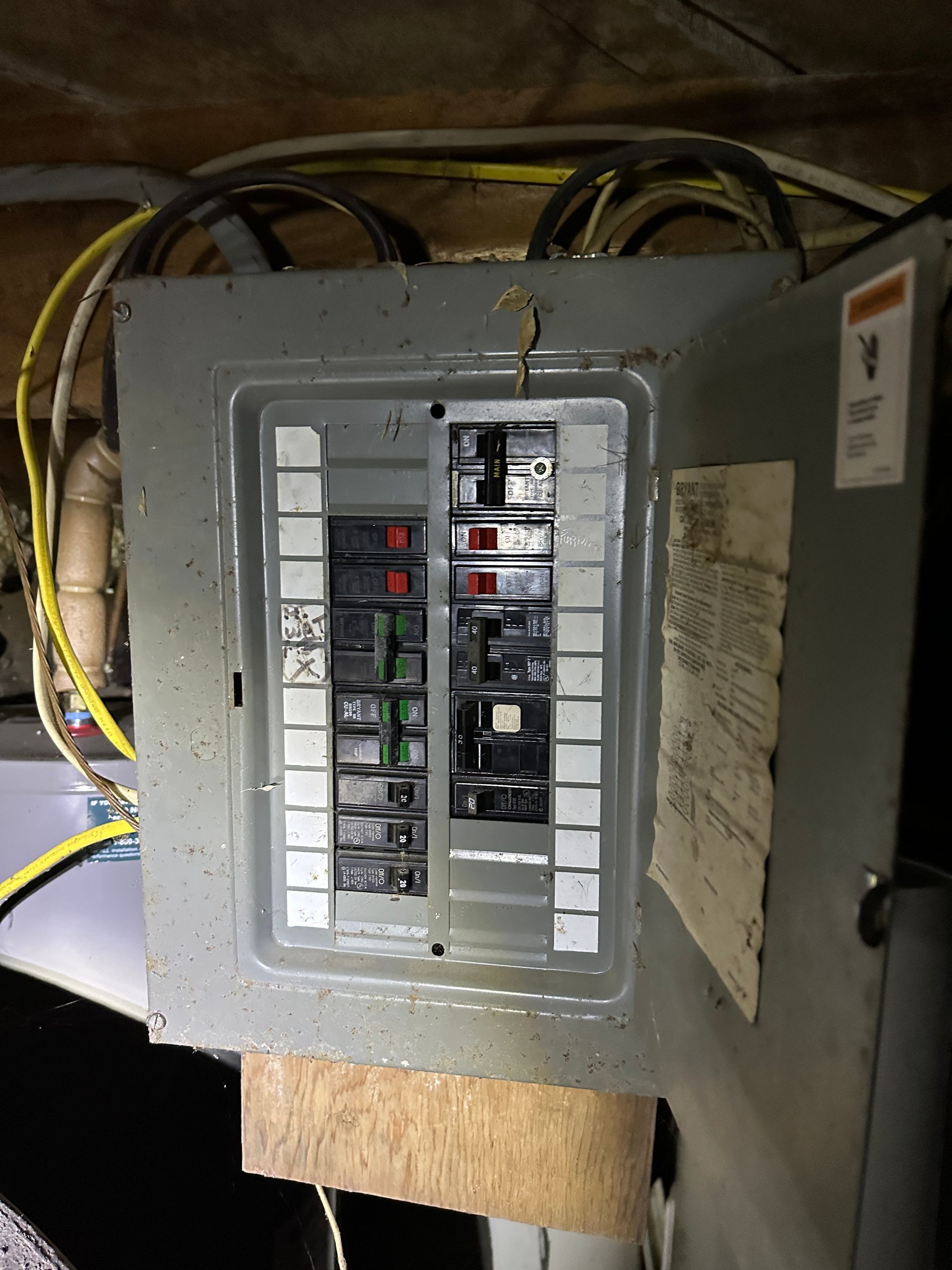 A grey electrical breaker panel with a door open, mounted on a wood board.