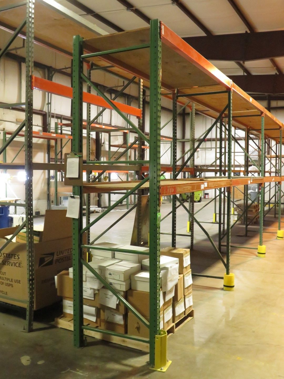 Warehouse shelving unit with pallets of boxes, green metal supports, wood shelves.