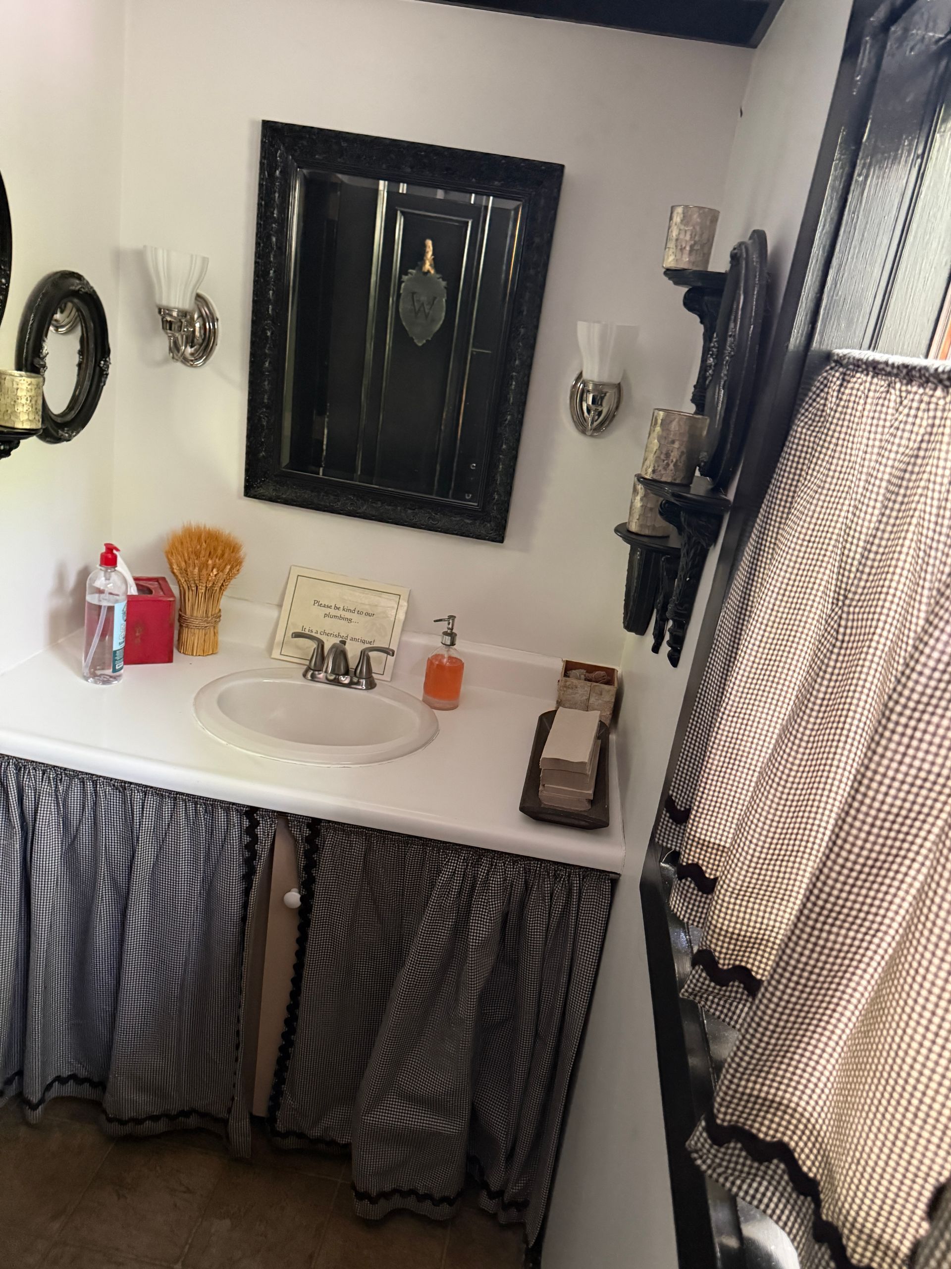 Bathroom vanity with white sink, black-framed mirror, patterned curtains, and wall sconces