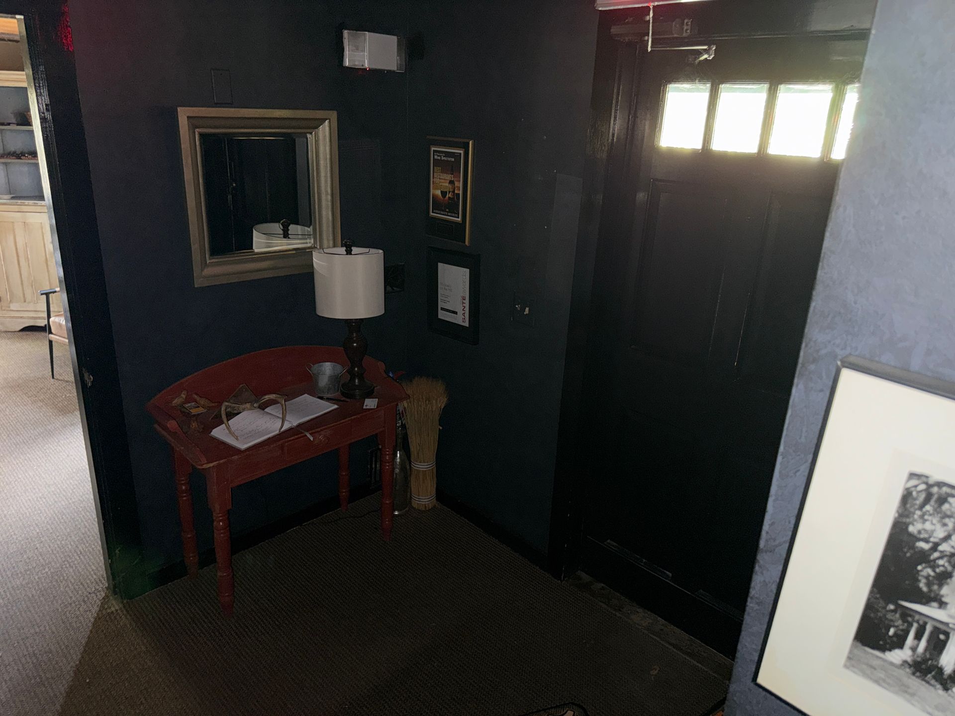 Small entryway with dark walls, a red table and lamp, a mirror, and a black front door with windows