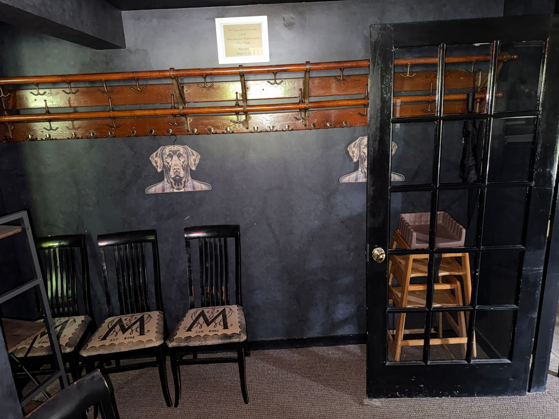 room with black chairs, wooden shelves, and a glass-front cabinet against a dark wall.