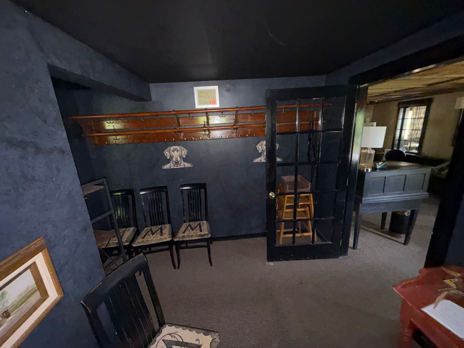 Dark blue dining room with black chairs, glass partition, and small table near a kitchen pass-through.