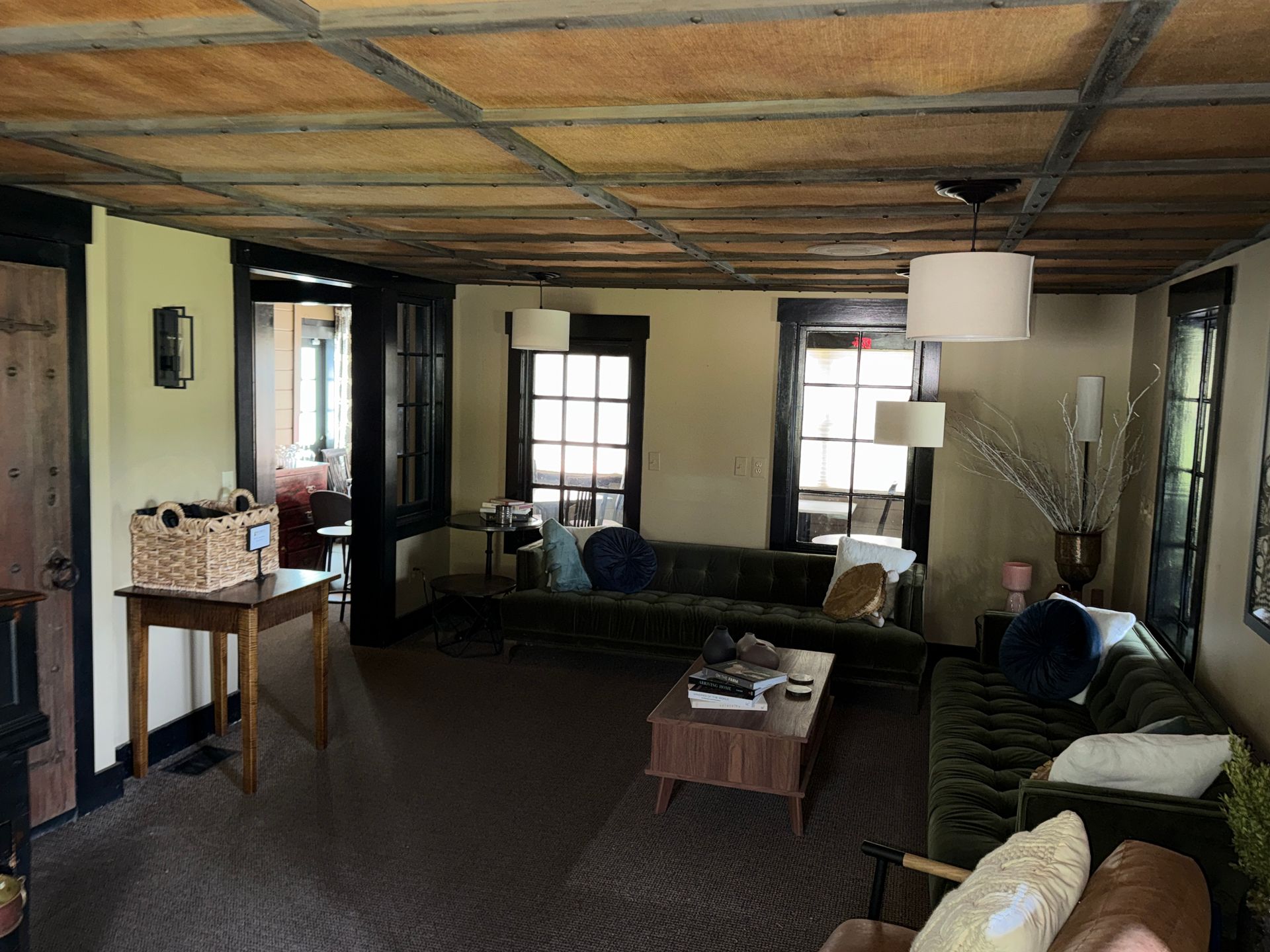 Cozy living room with green couch, wooden ceiling, large windows, and small coffee table