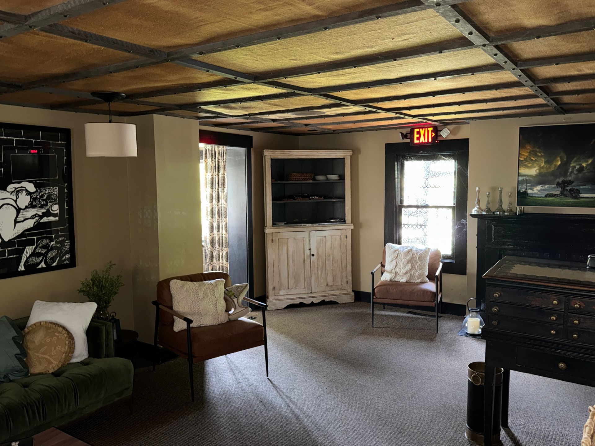 Cozy rustic room with wooden ceiling, upholstered chairs, cabinet, and a door with an EXIT sign.