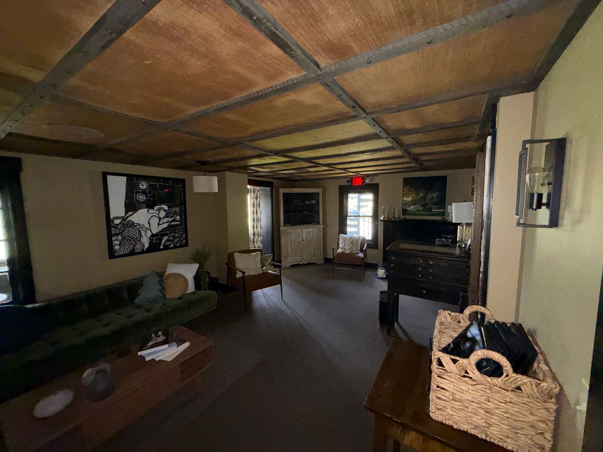 Cozy lounge with green sofas, wooden beams, coffee table, and a cabinet near a doorway.