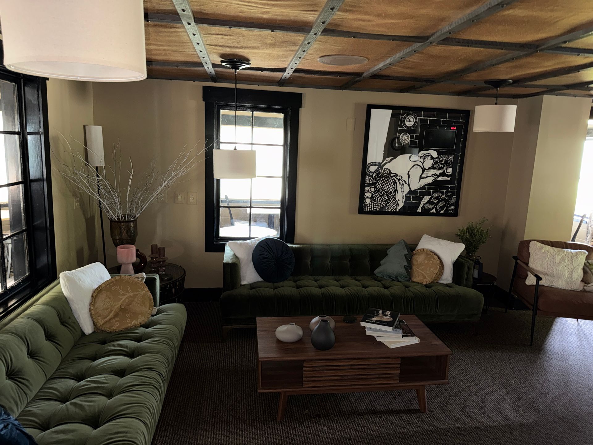 Cozy living room with green sofas, wooden coffee table, framed wall art, and large windows