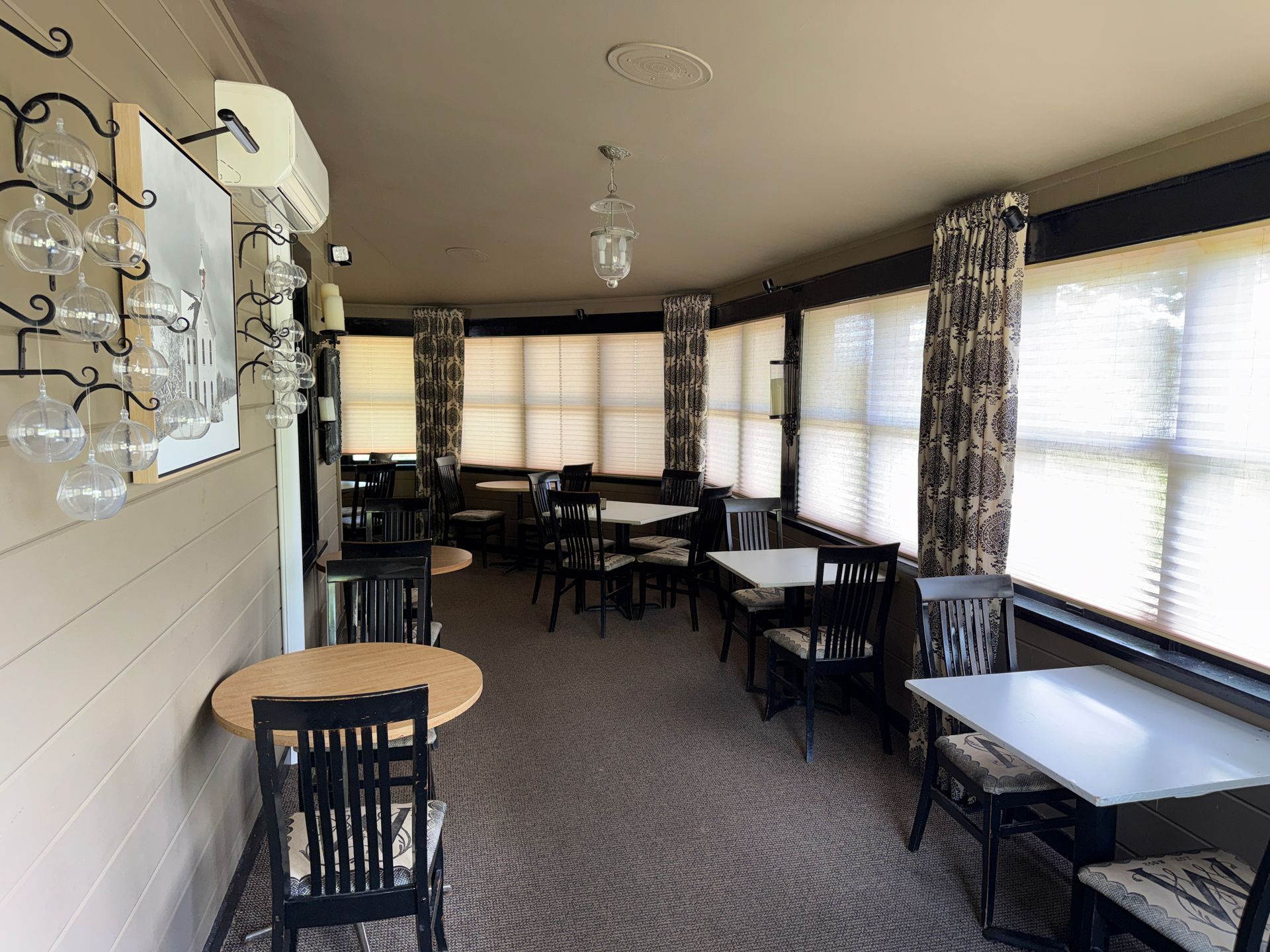 Empty restaurant dining area with tables, chairs, and large windows with curtains