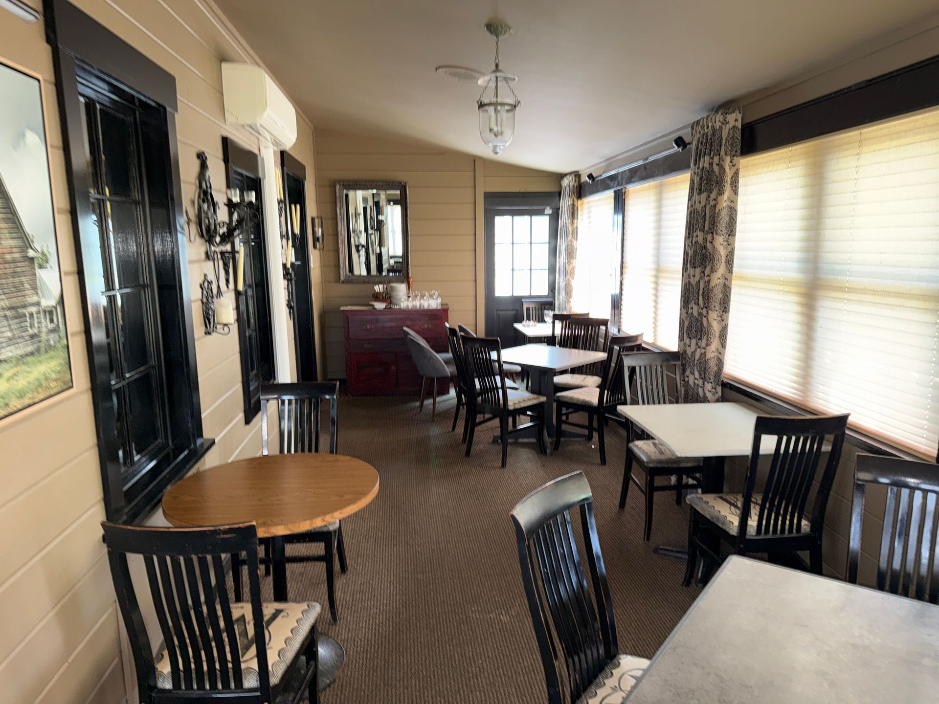 Empty cafe dining room with wooden tables and chairs, windows with blinds, and a bar area at the back