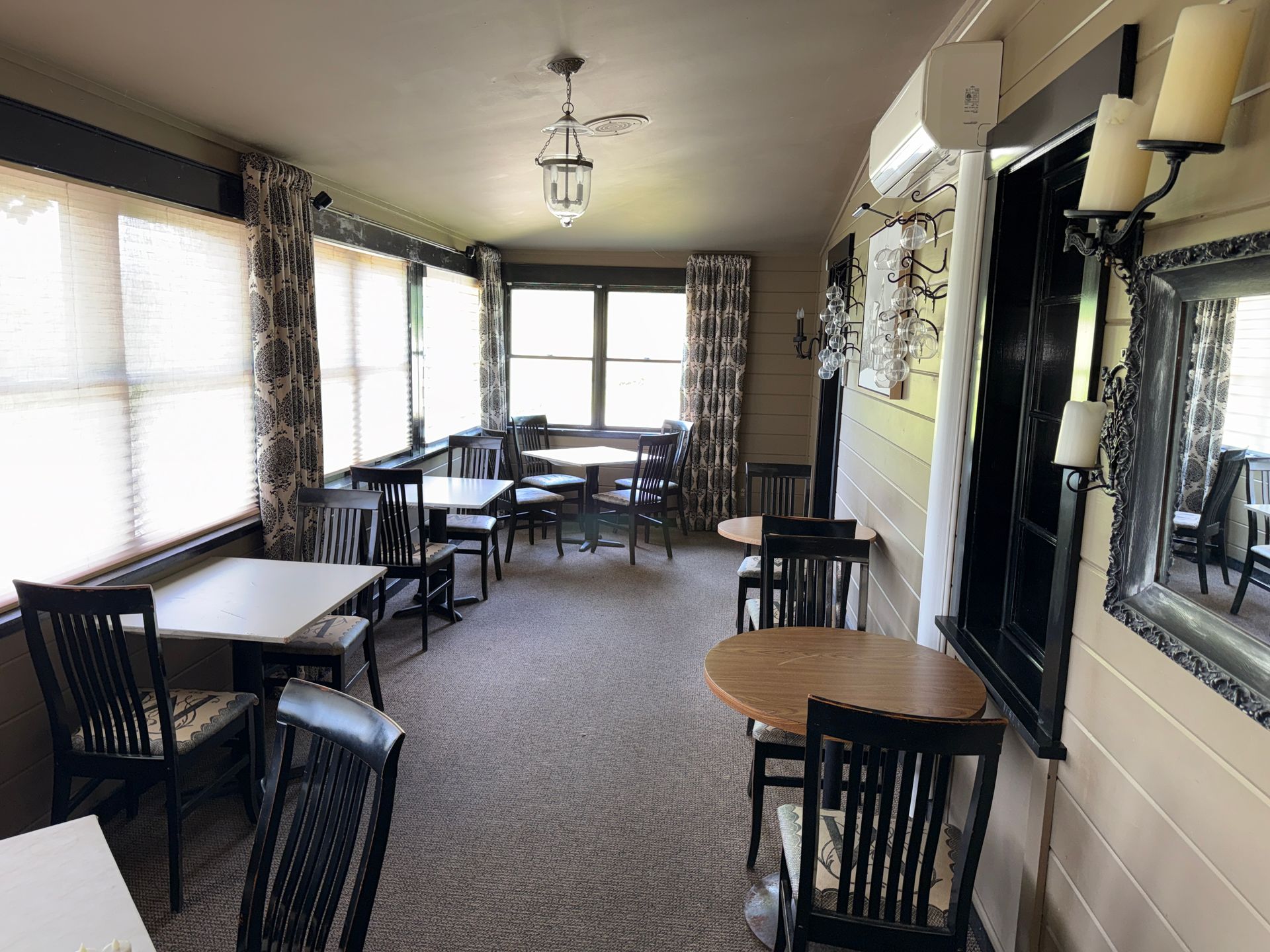 Empty café seating area with white tables, black chairs, large windows, and carpeted floor.