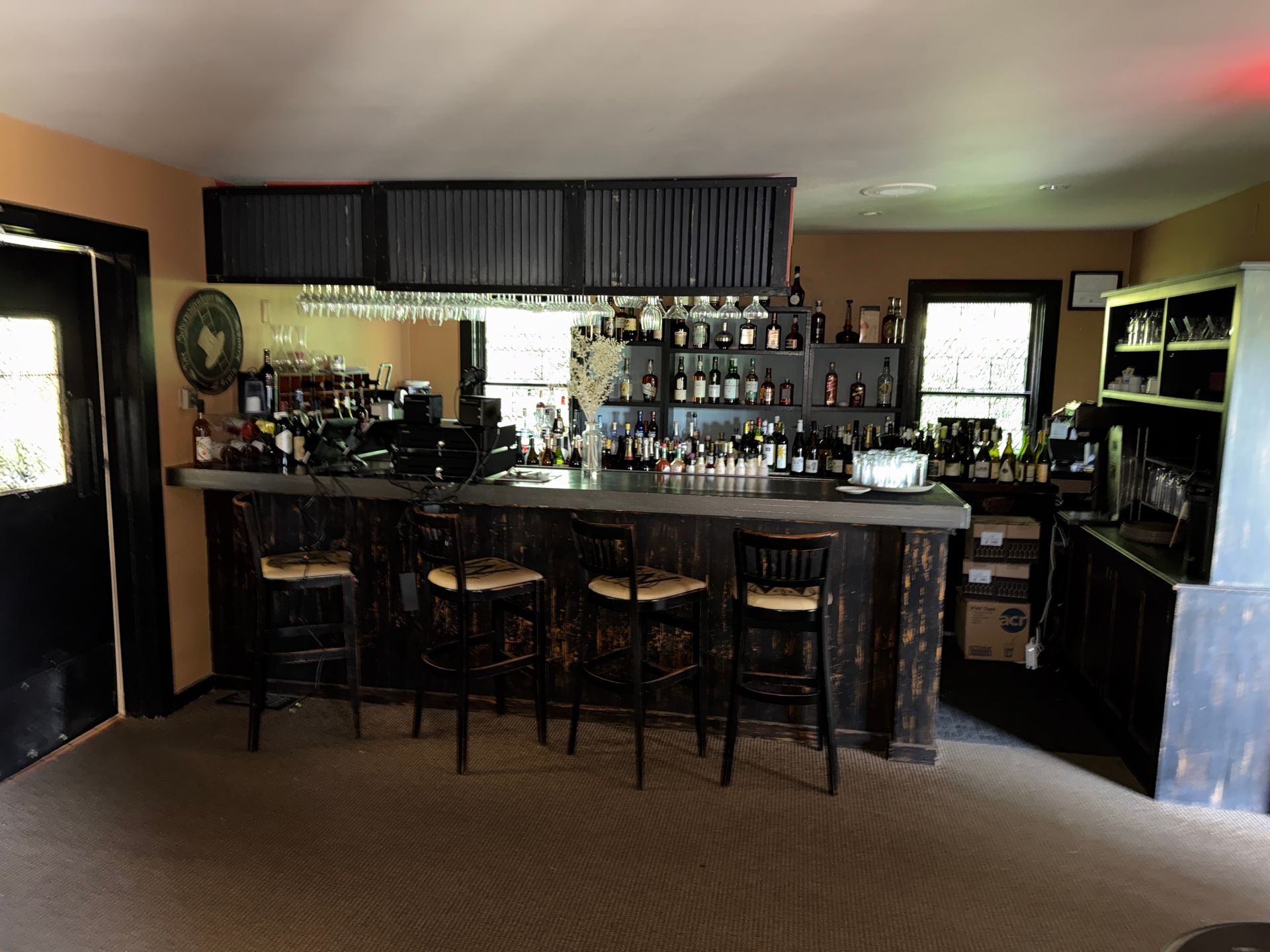 Empty bar interior with stools, bottles on shelves, and dark wood counters under soft lighting