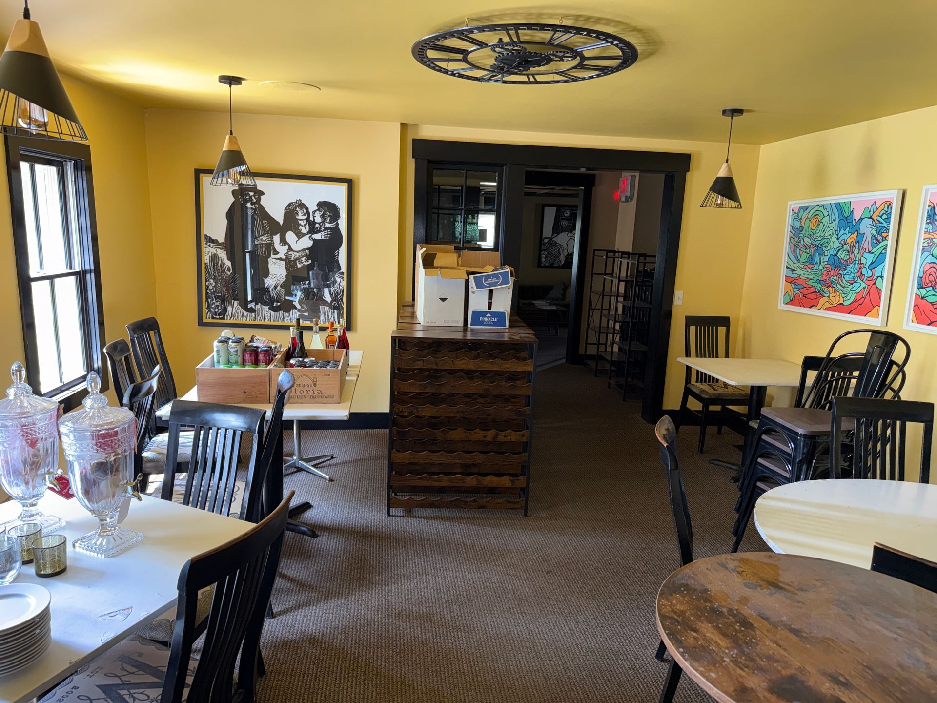 Cozy café interior with tables, chairs, warm yellow walls, artwork, and a central service counter