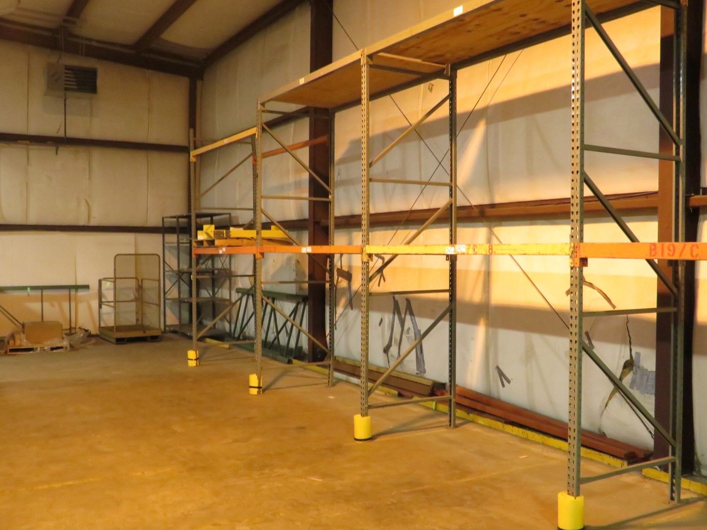 Metal shelving units inside a warehouse. Yellow floor with wooden shelves, metal supports and safety caps.
