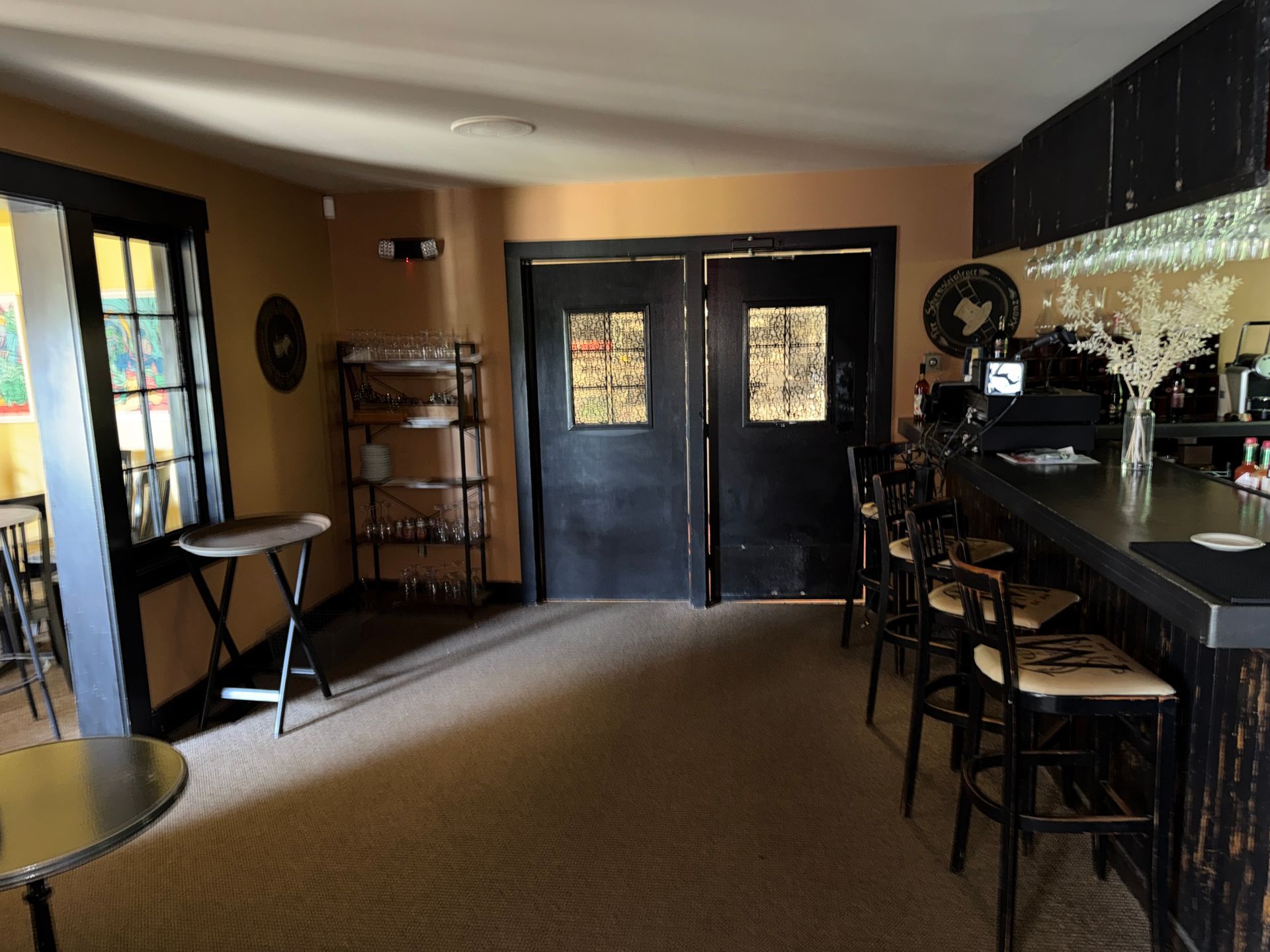 Empty café interior with black double doors, bar stools, and tables along the walls