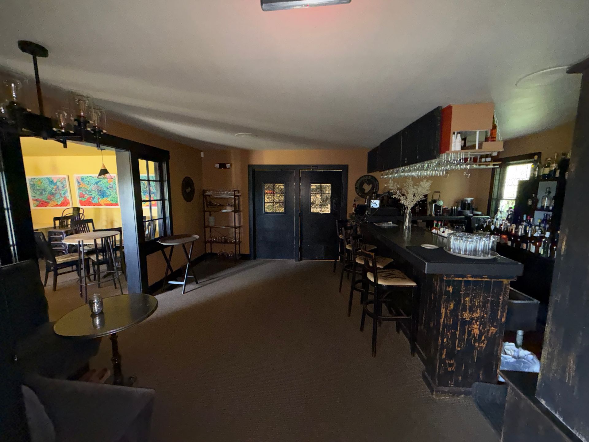 restaurant interior with a long bar, stools, tables, and double doors at the back.