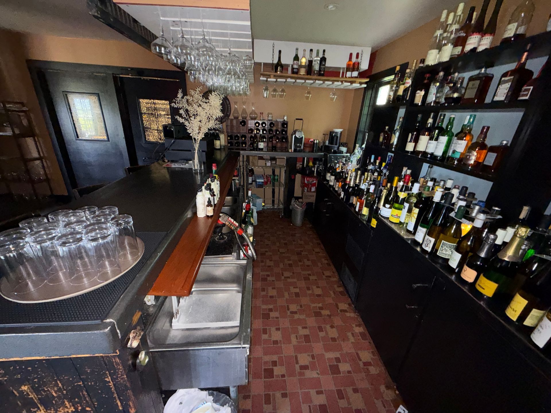 Wine bar interior with shelves of bottles, a counter, and hanging glasses in warm lighting