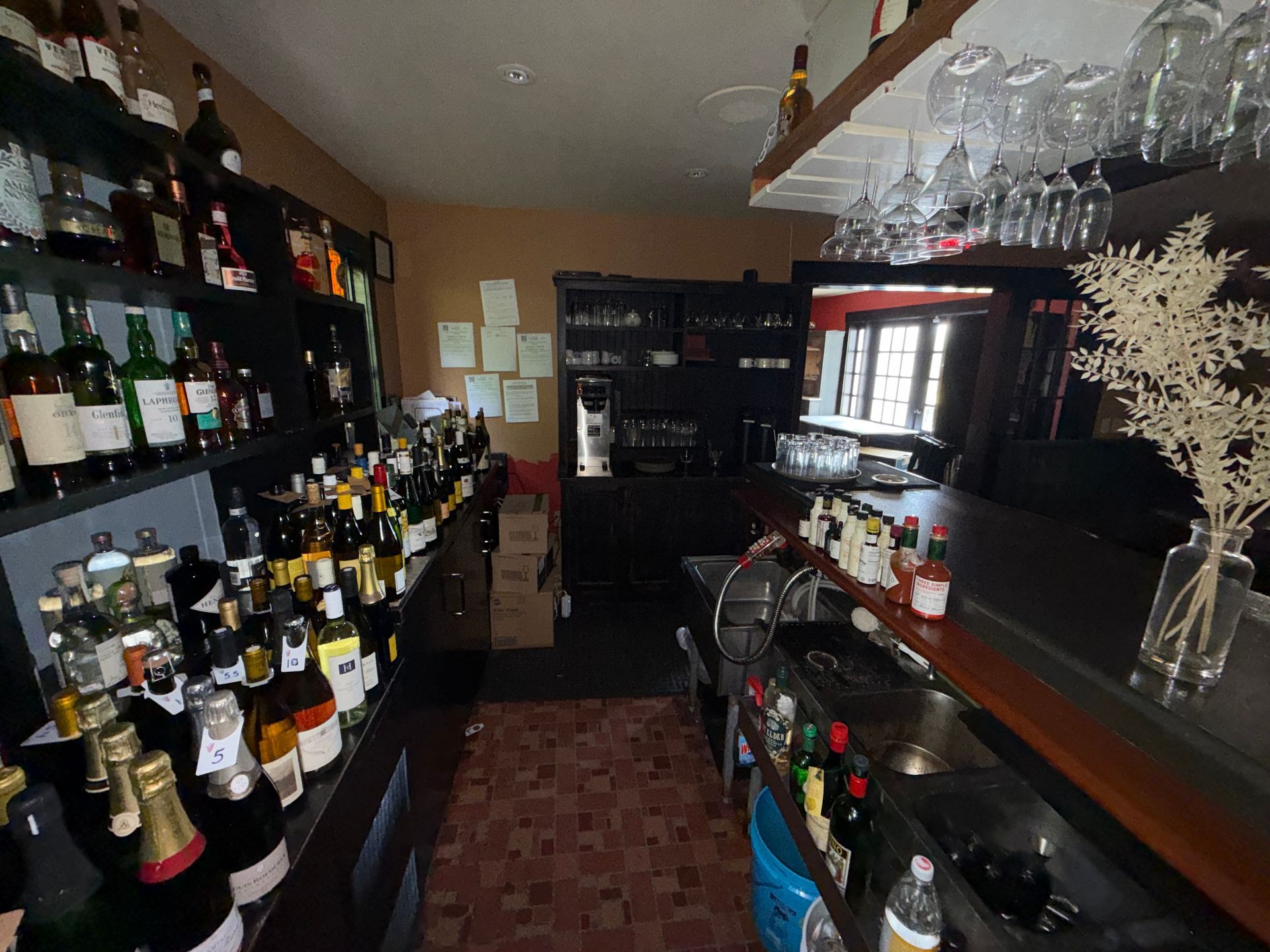 Small wine bar interior with shelves of bottles, hanging glassware, and a wooden counter.
