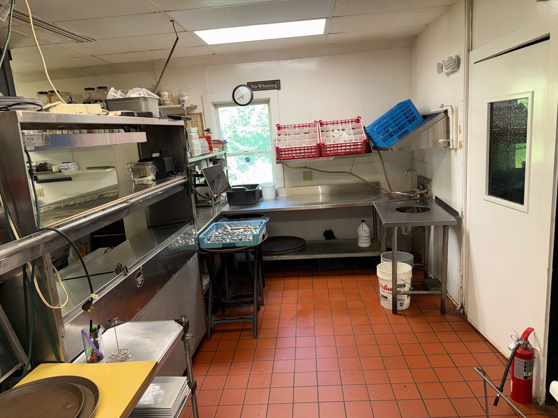 Small commercial kitchen with stainless shelves, prep tables, sink, and tiled floor under fluorescent lights