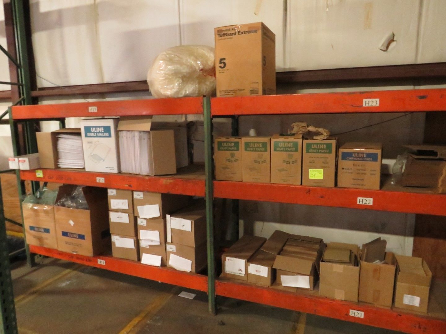 Shelving unit filled with various cardboard boxes and a roll of plastic in a warehouse.