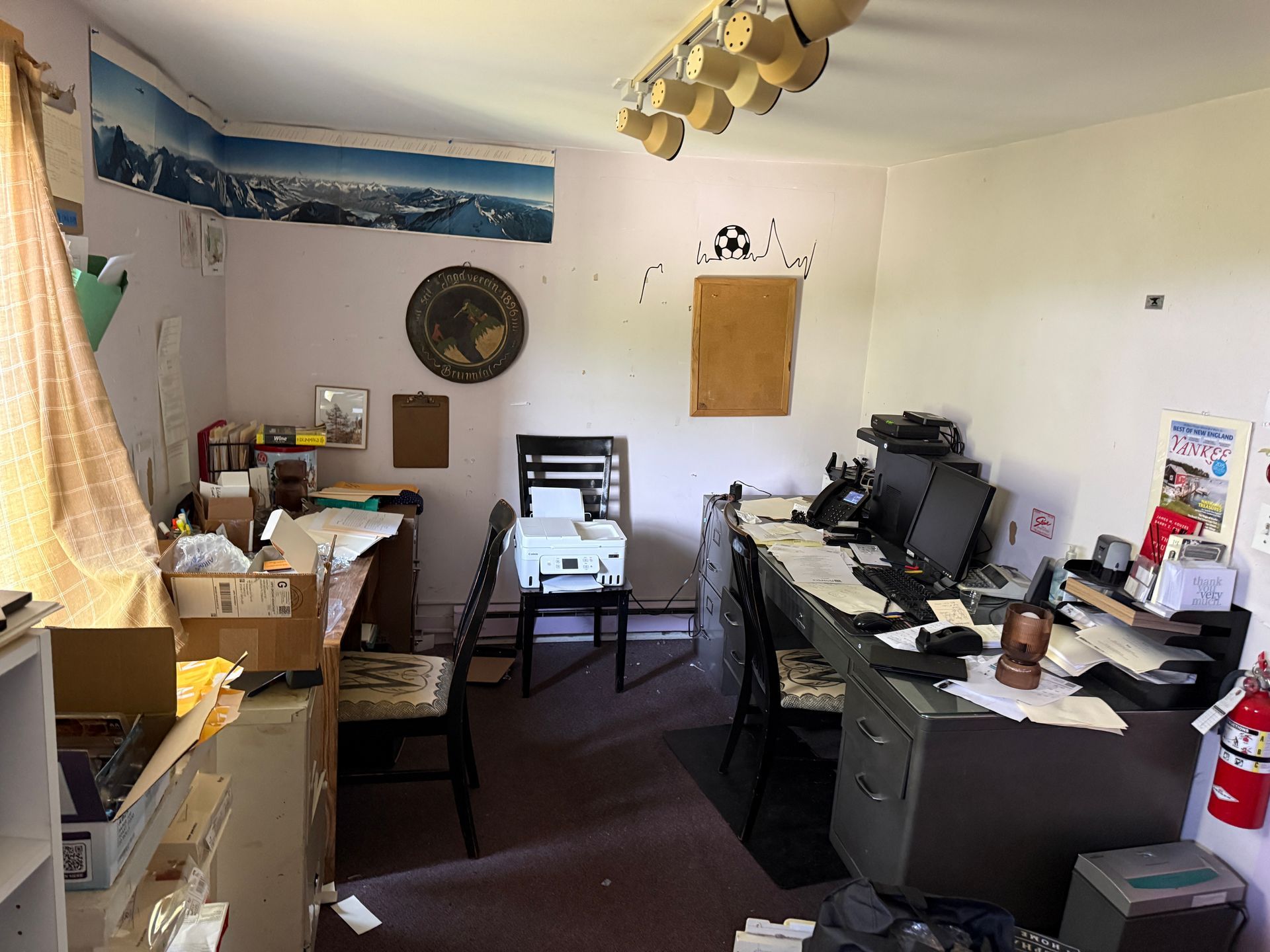 home office with desks, computer monitors, papers, and chairs in a small room.
