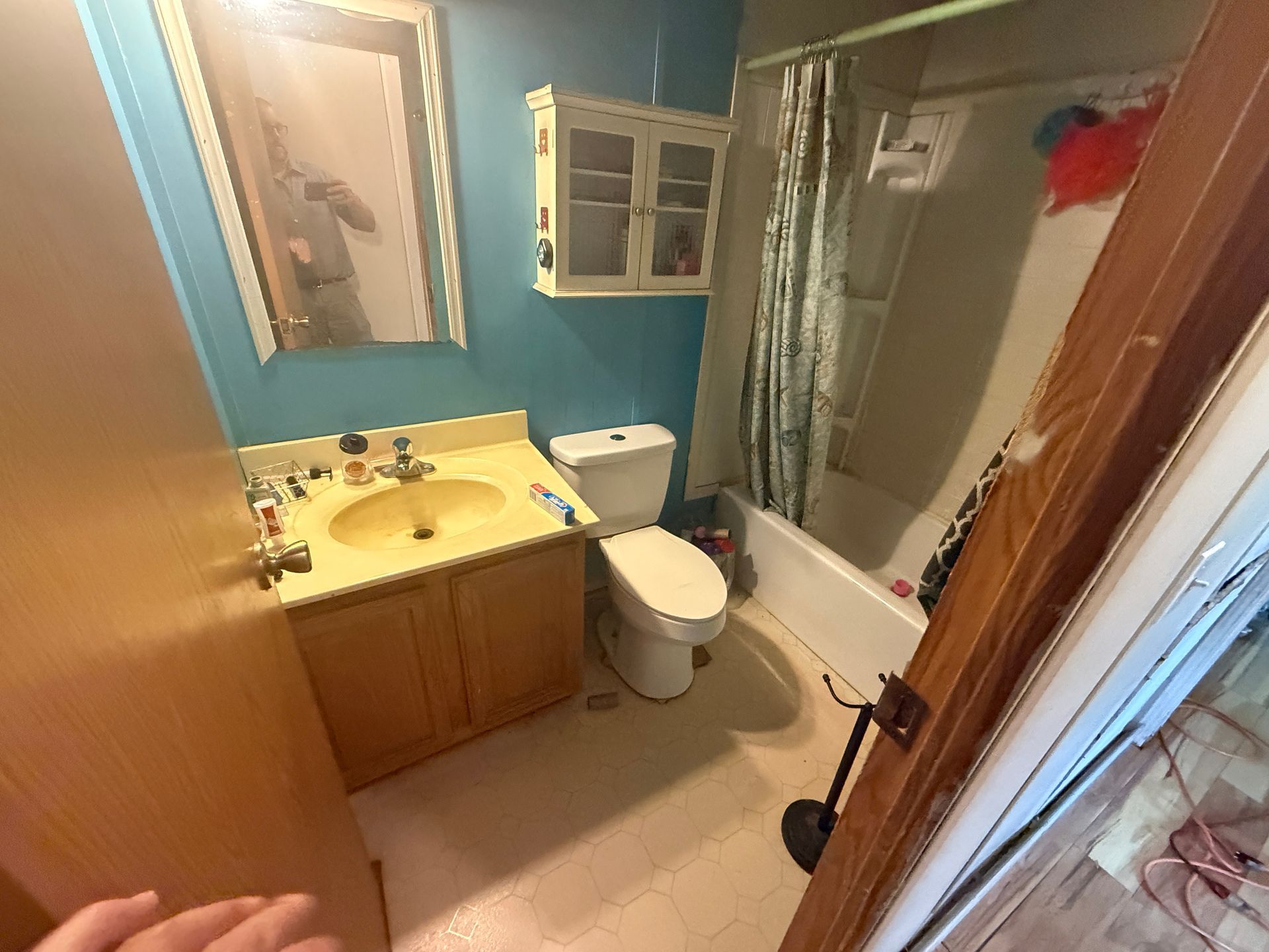 Blue bathroom with yellow sink, toilet, tub, mirror, and shower curtain, seen through a doorway.