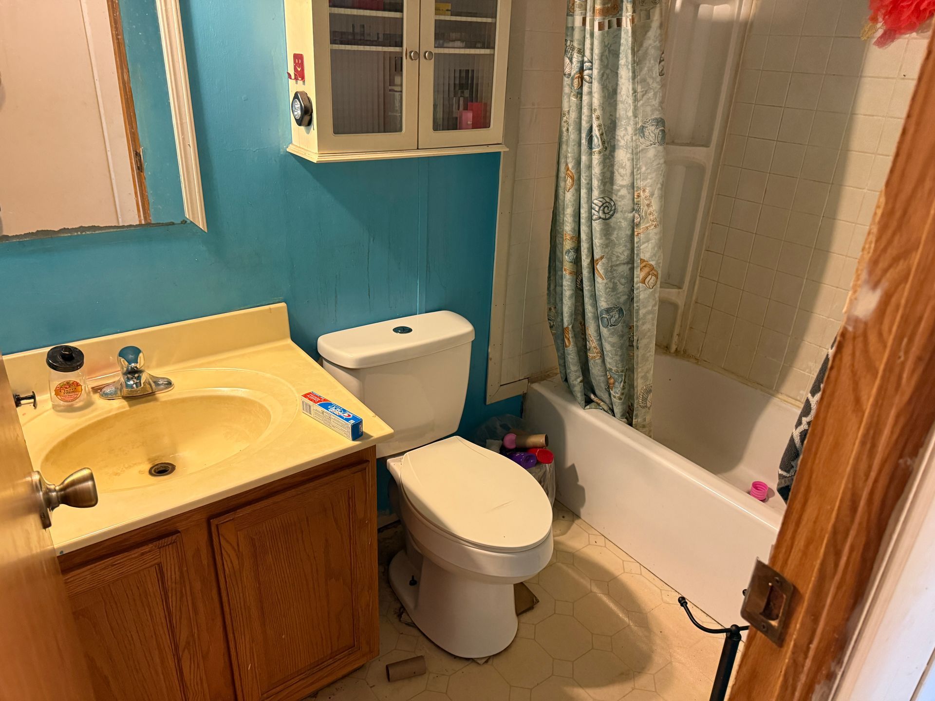 Small bathroom with a sink, toilet, and bathtub, featuring blue walls and wood trim.
