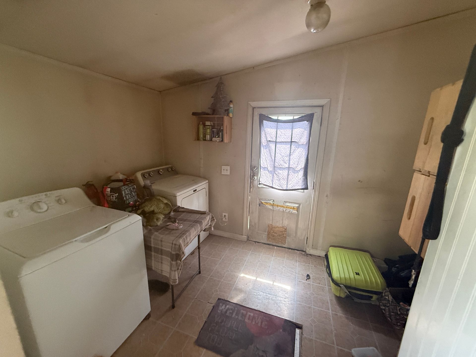 Small laundry room with washer, sink, door, window, chair, and storage cabinet.