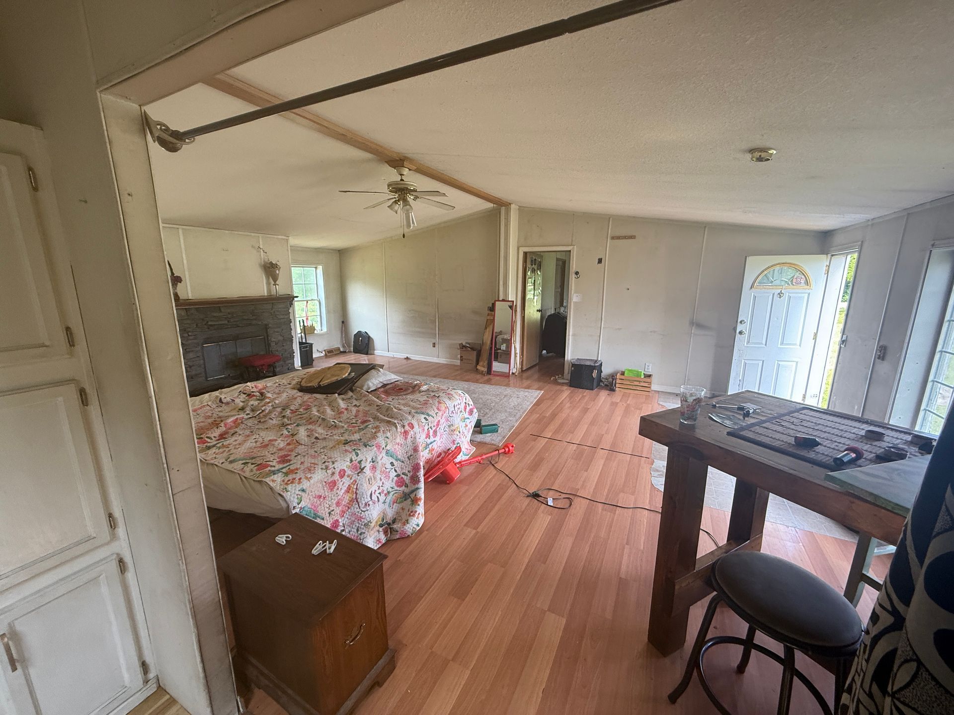 Small bedroom with floral bedspread, wood floor, desk, chair, and open door near a window.