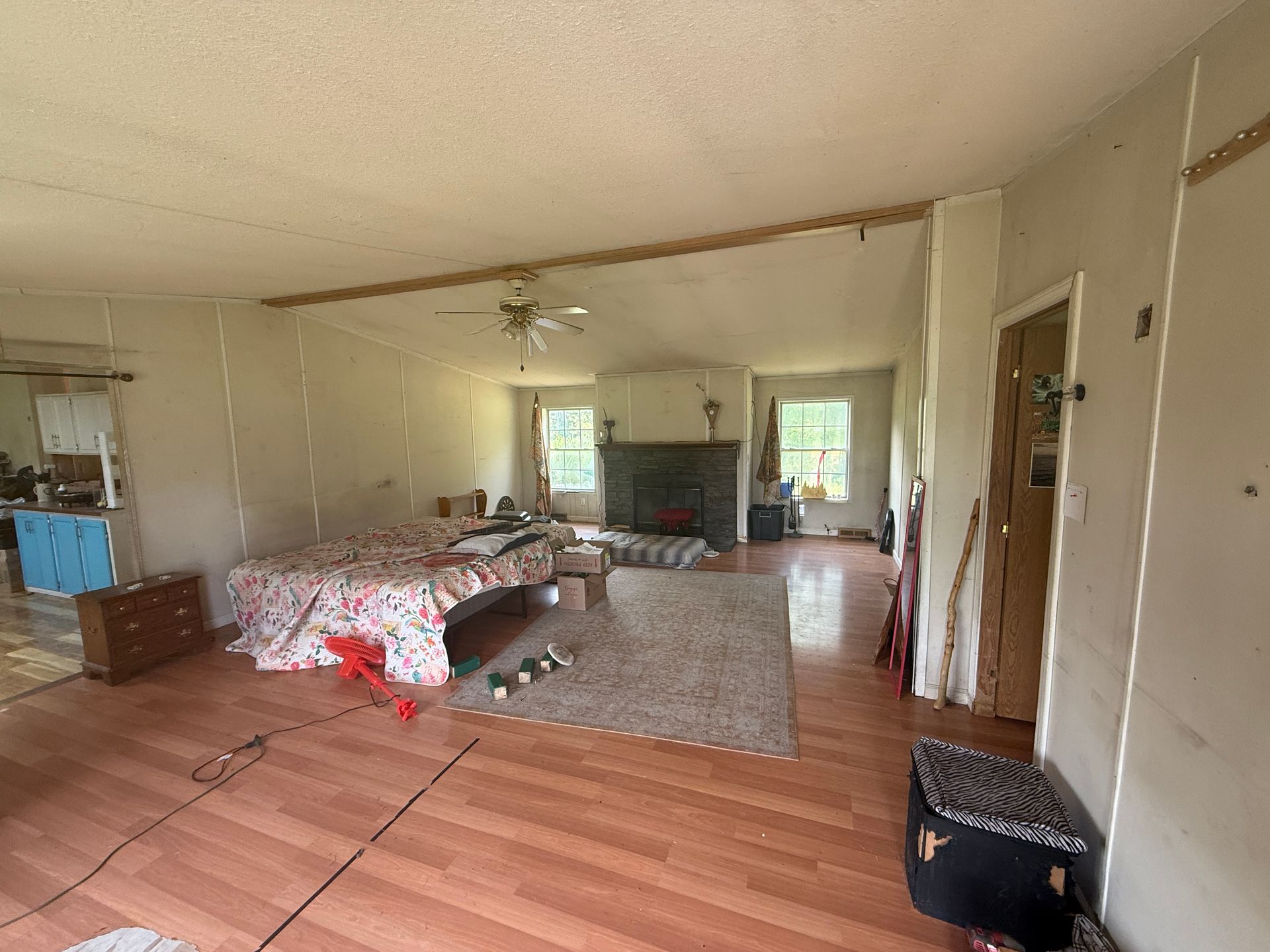 Spacious living room with a bed, couch, and dresser on wood floors, viewed from an open doorway.