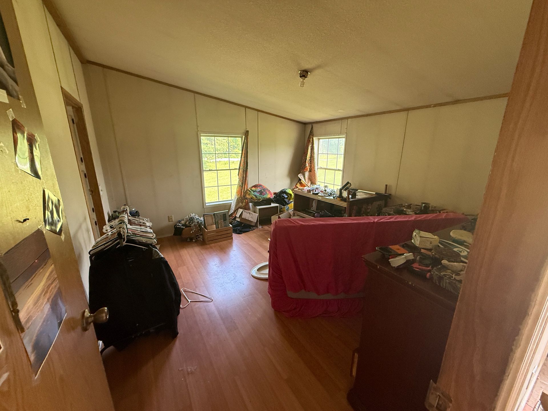  room with wood floors, red couch, and two windows letting in daylight.