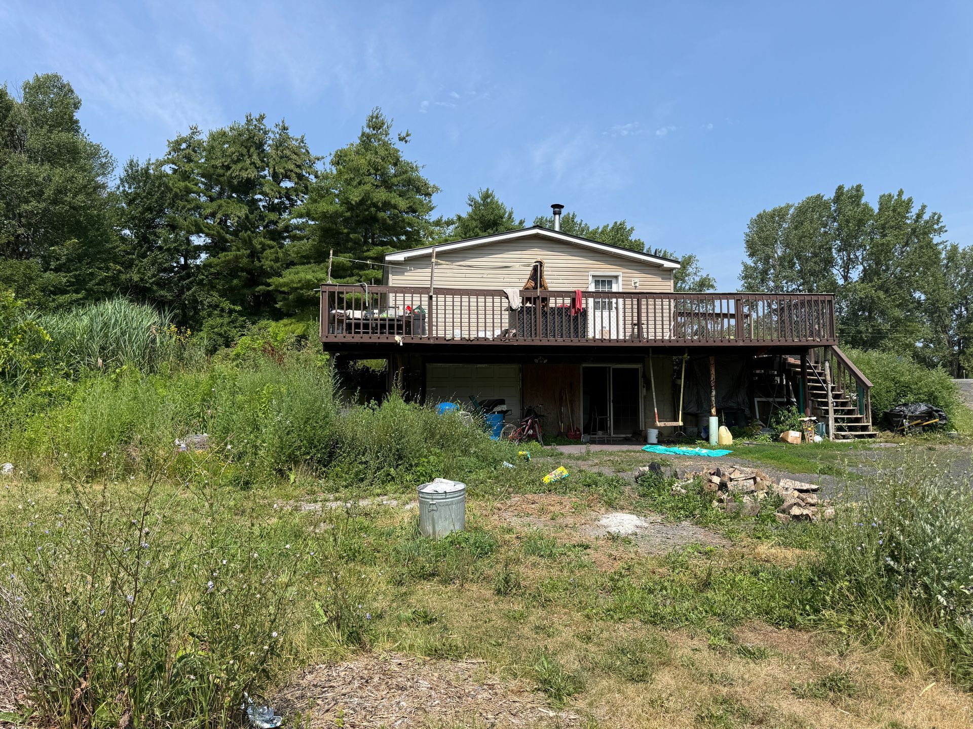 A small house with a wooden deck sits on a grassy hillside under a clear blue sky.