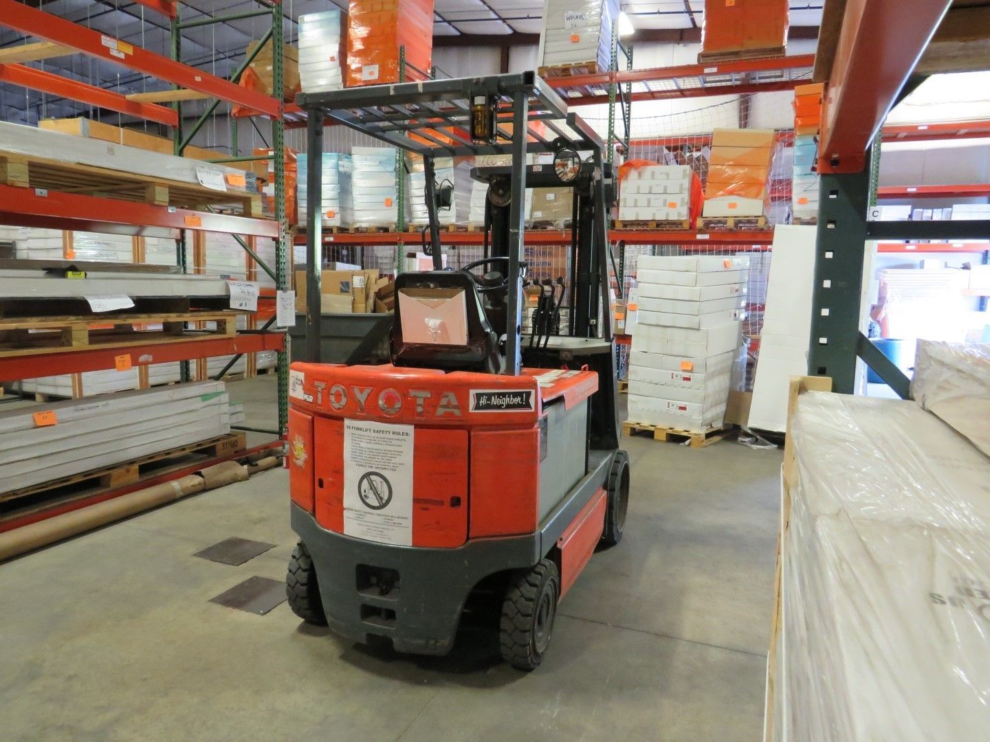 A red and gray Toyota forklift in a warehouse with shelving and packaged goods.