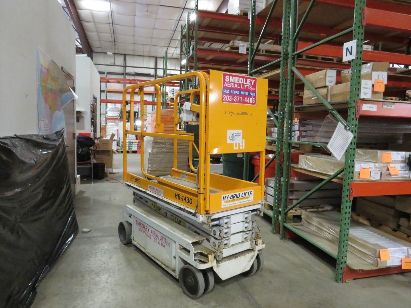 Yellow and white scissor lift in a warehouse aisle next to shelving.