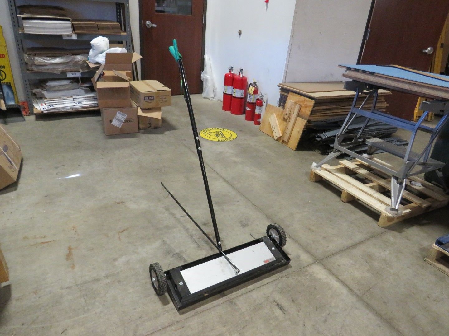 Magnetic sweeper with a handle and wheels in a warehouse.