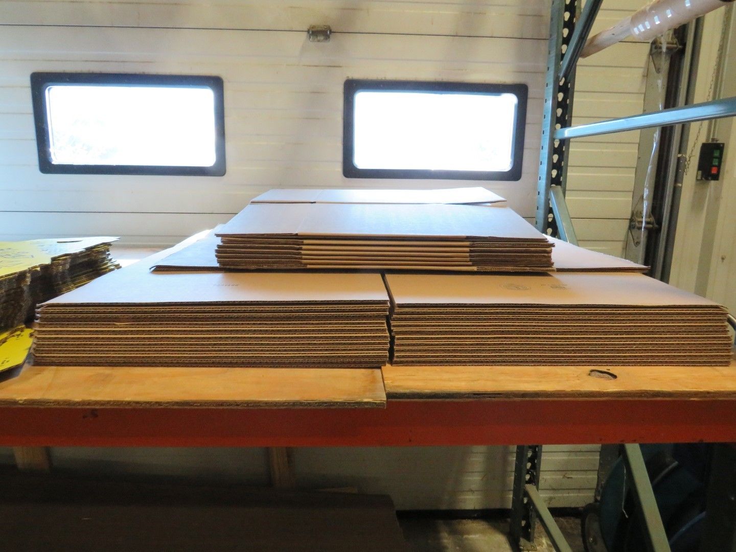 Cardboard sheets stacked on a shelf in a warehouse, with windows in the background.