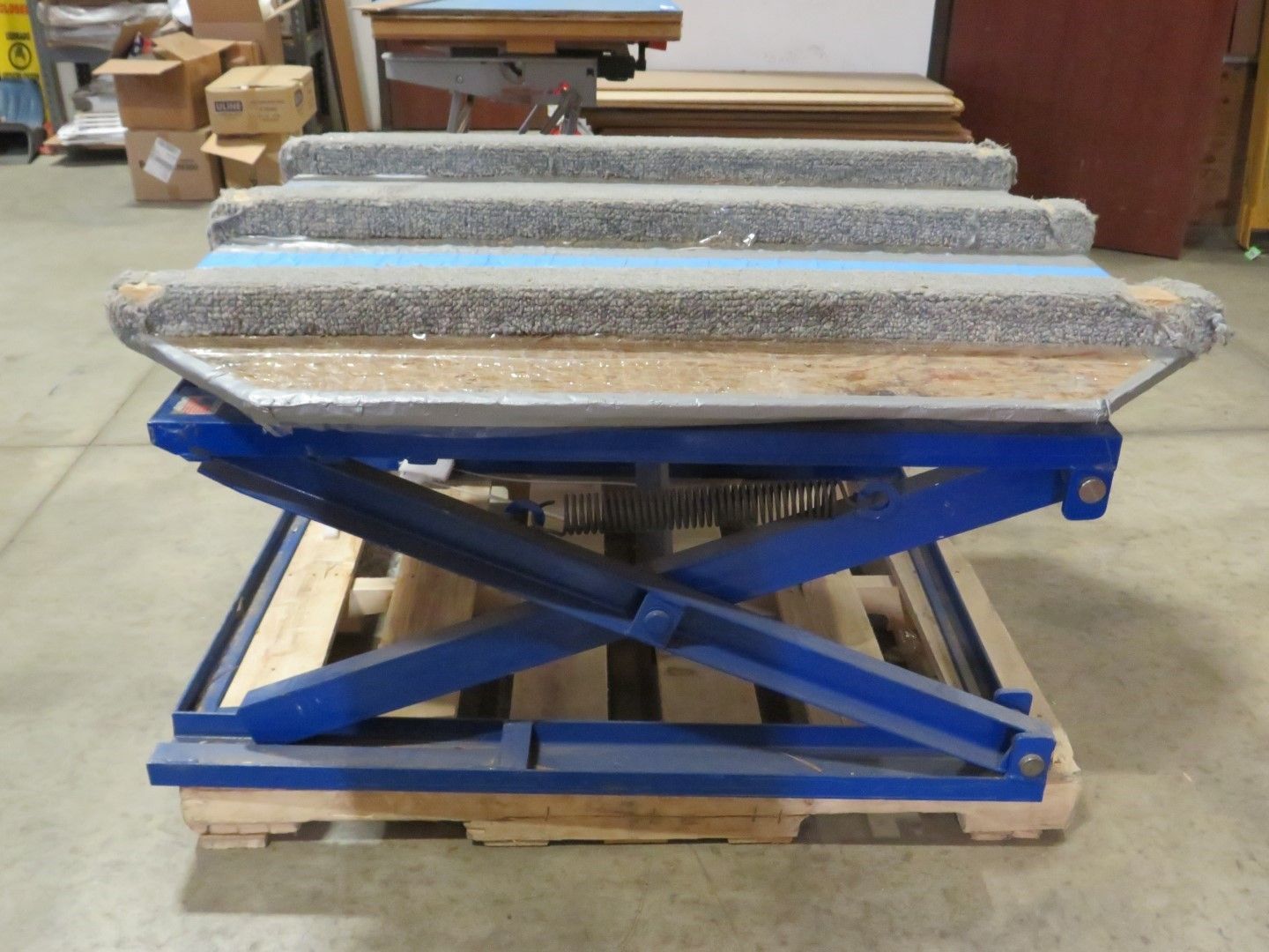 Blue scissor lift holding a set of concrete steps on a wooden pallet.
