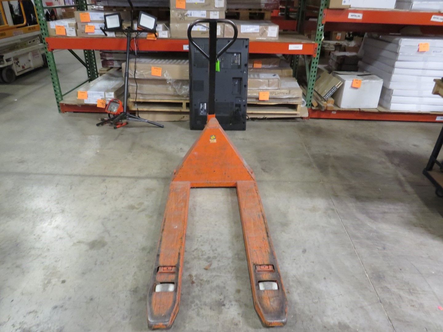Orange and black pallet jack in a warehouse aisle.