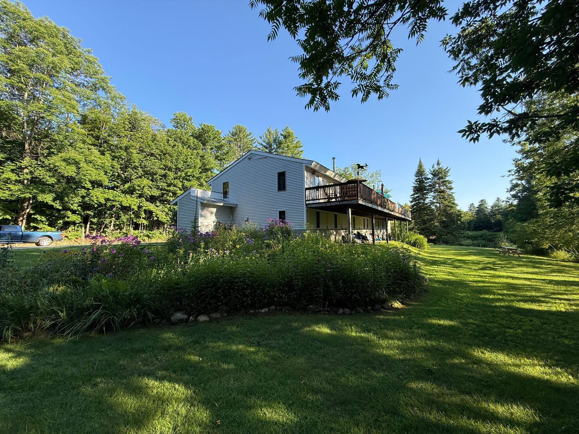 White farmhouse with a porch amid green lawn and trees under a bright blue sky