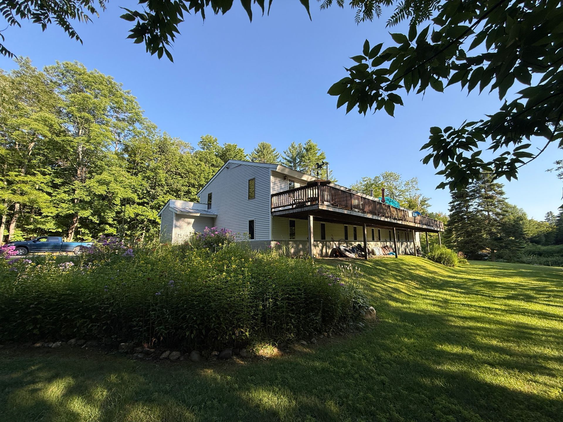 Large house with a wraparound porch behind a hedge on a sunny green lawn