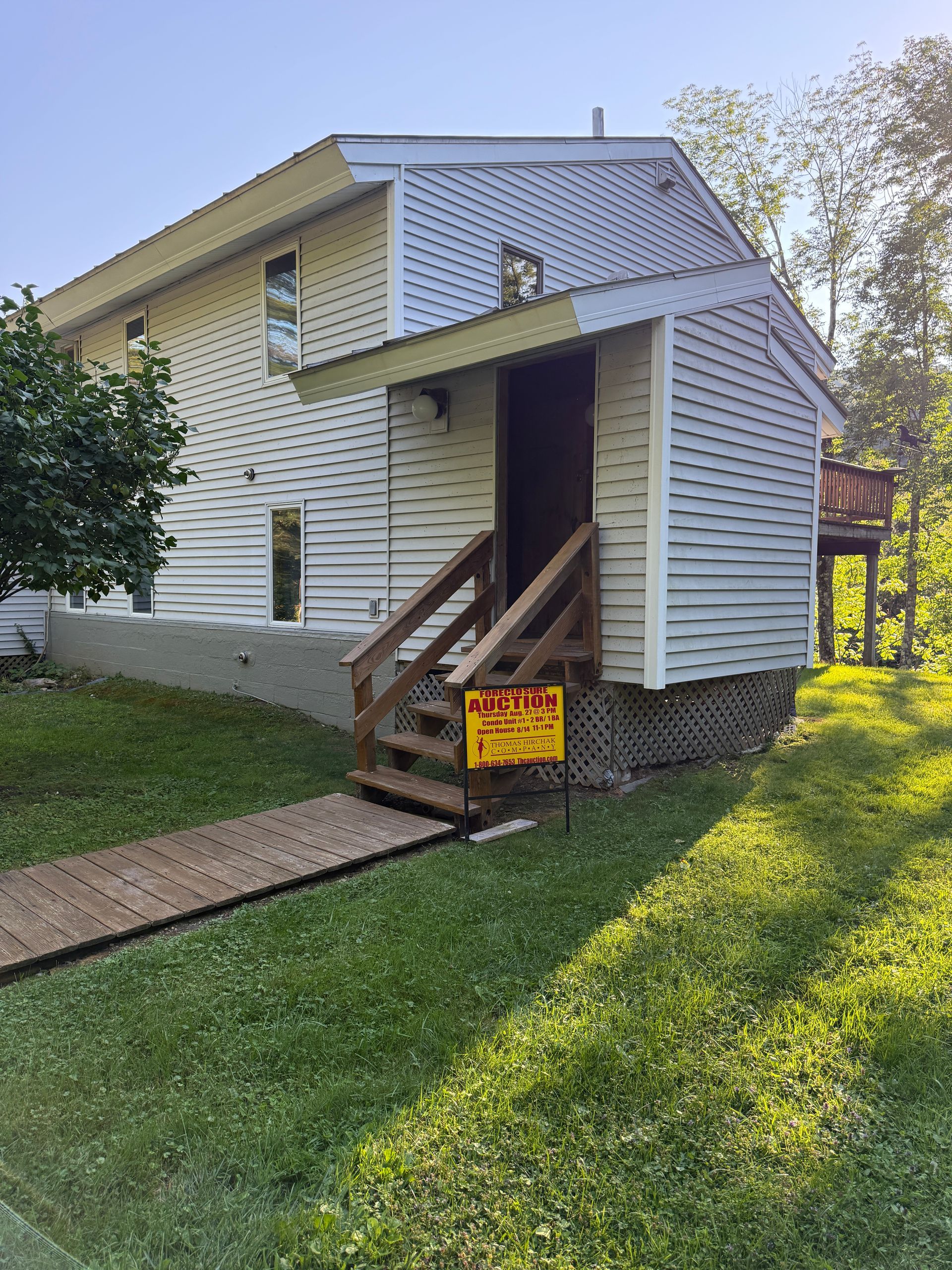White house exterior with a small covered porch, stairs, and a yellow sign on the railing.
