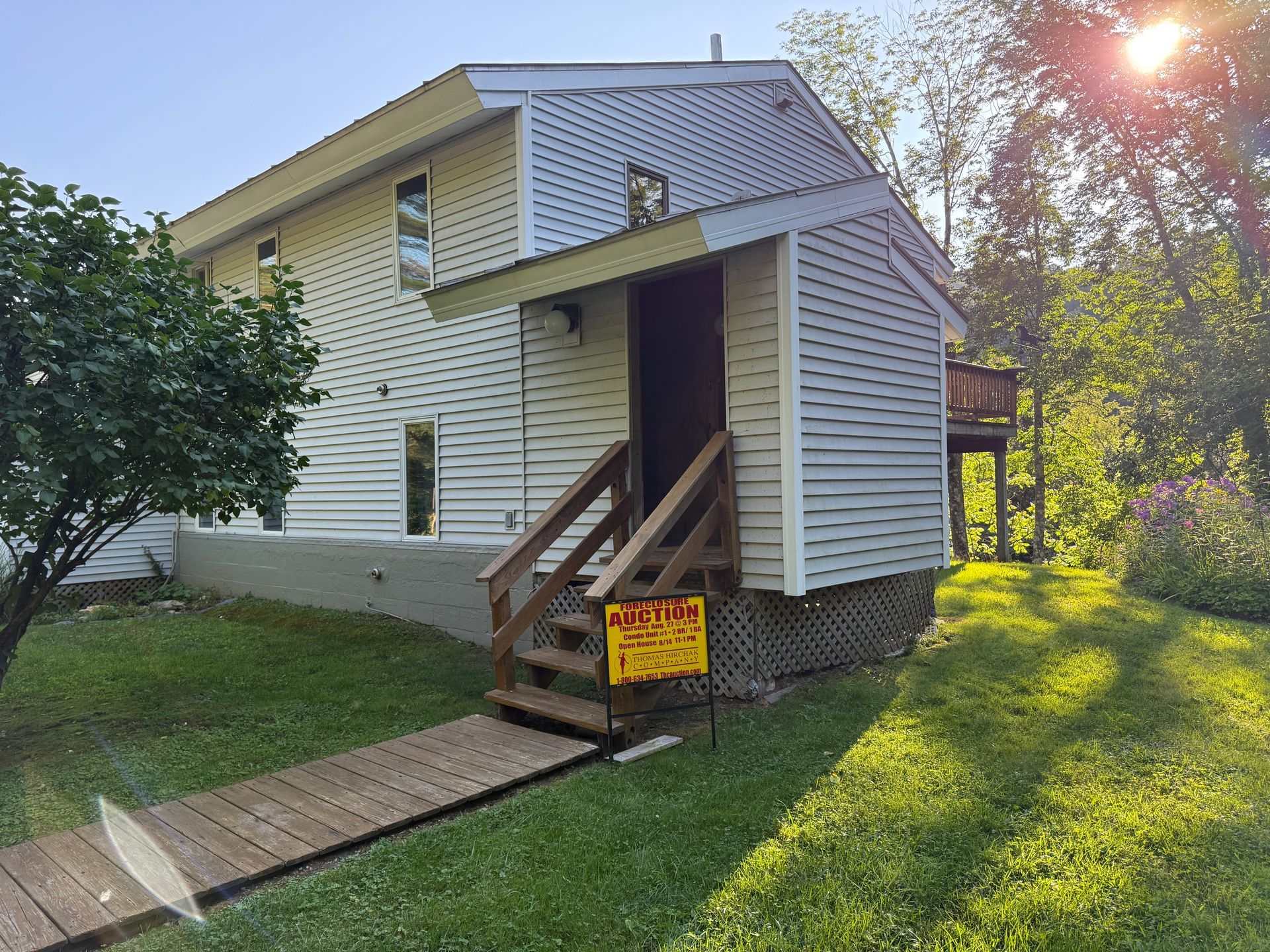 White house with wooden stairs and a yellow sign in the yard at sunset
