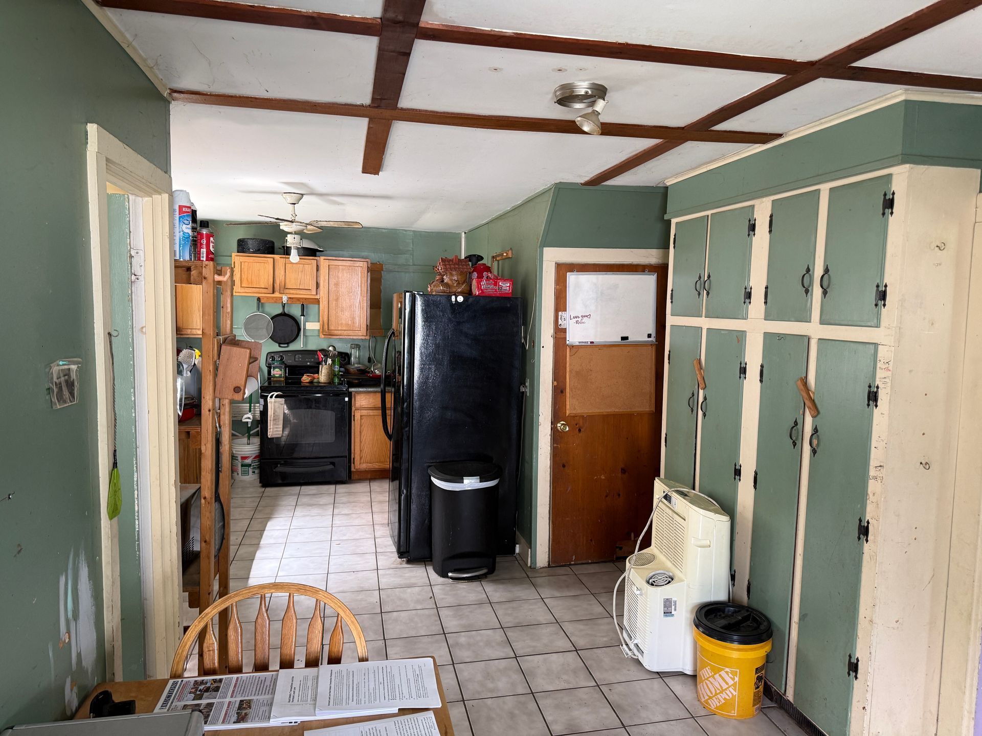 Narrow kitchen hallway with green cabinets, a black fridge, tiled floor, and a small table in the foreground