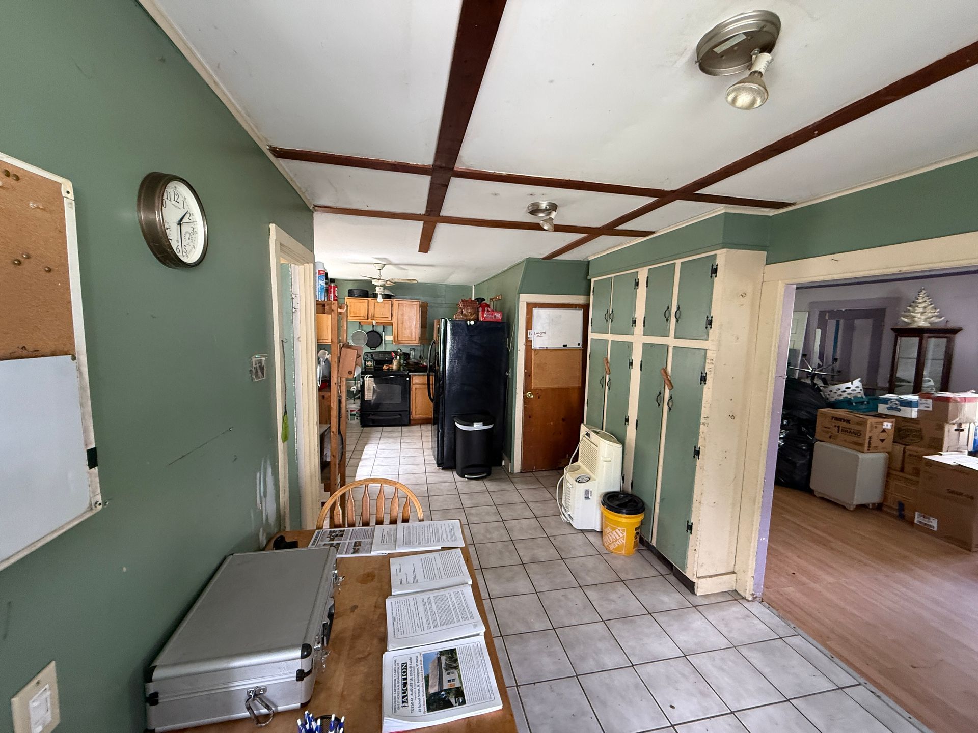 Narrow kitchen and hallway with green walls, white tile floor, black fridge, and a cork board on the left wall