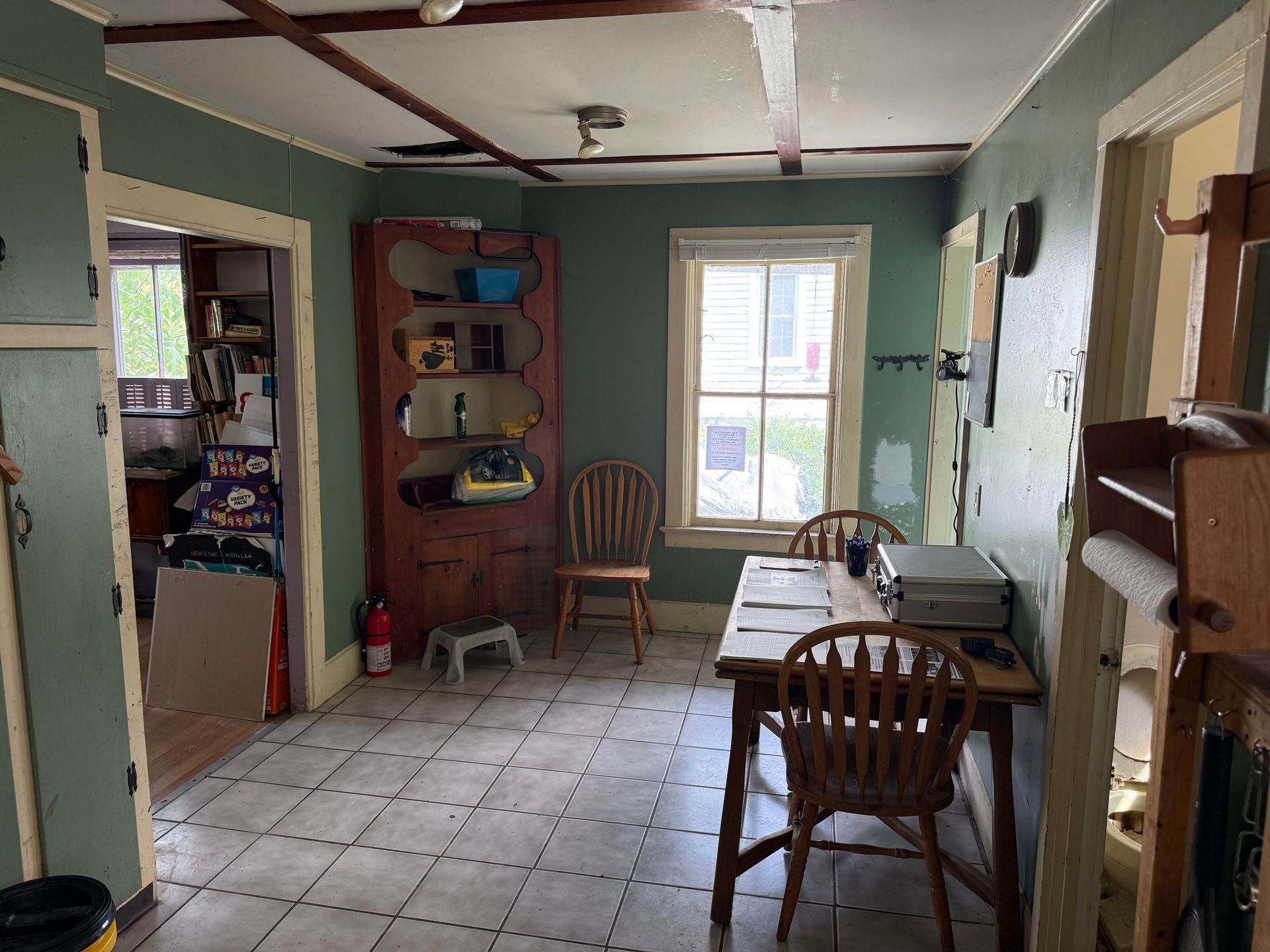 kitchen-dining room with tiled floor, green walls, wooden chairs, and a window at the back.