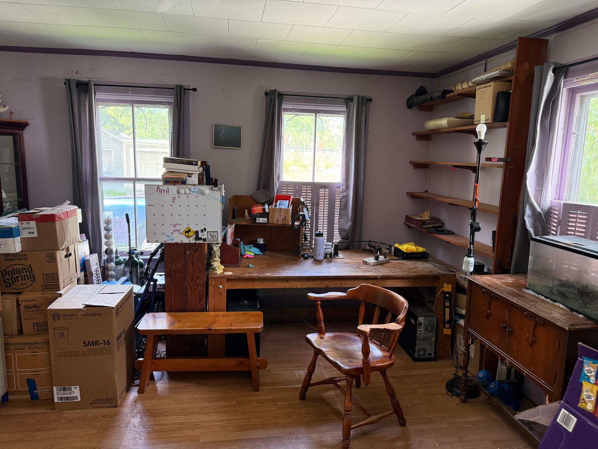 room with boxes, a worktable, shelves, chairs, and three windows letting in daylight.