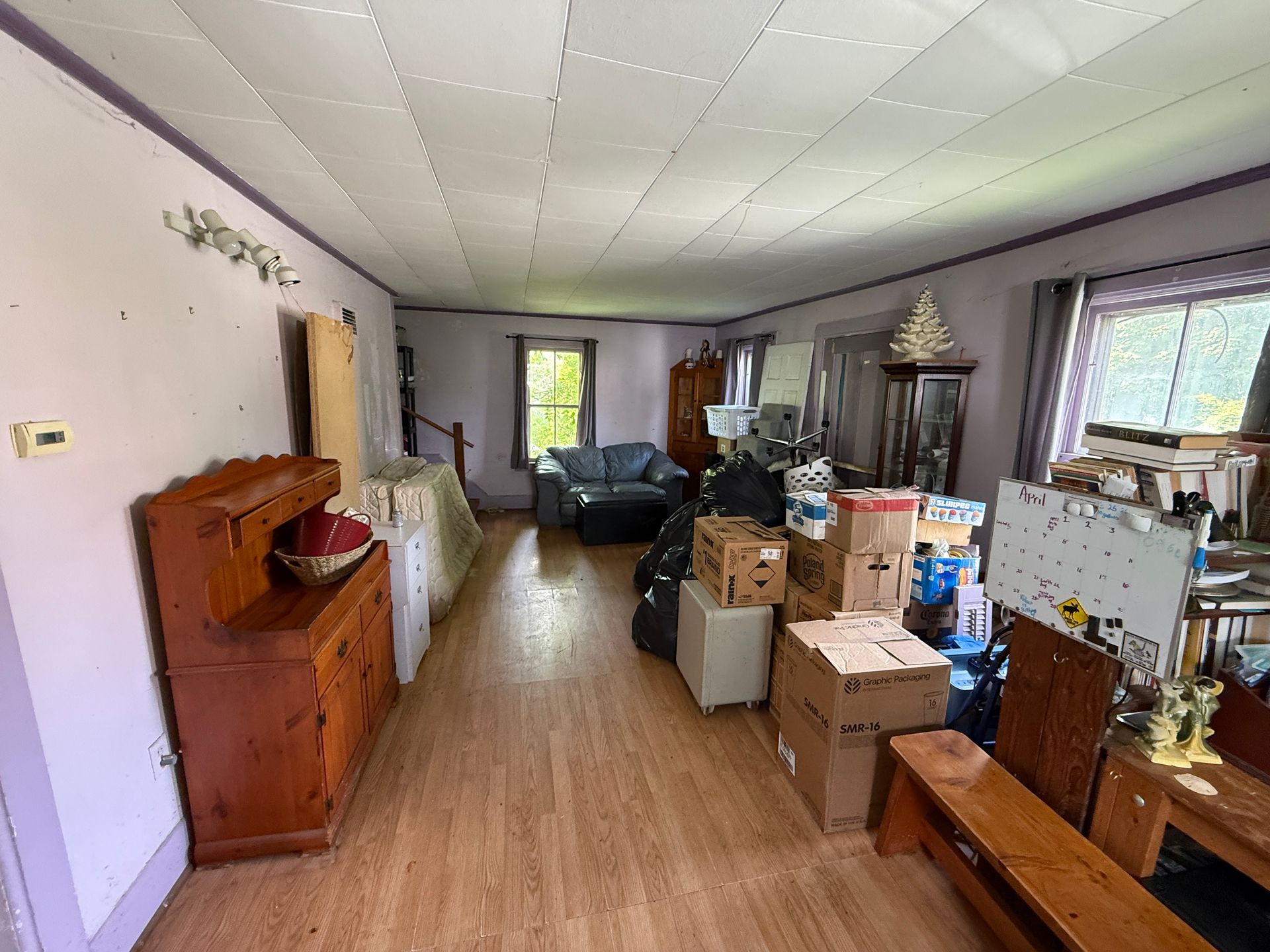Long room with boxes, furniture, and a couch along a wood floor and white ceiling.