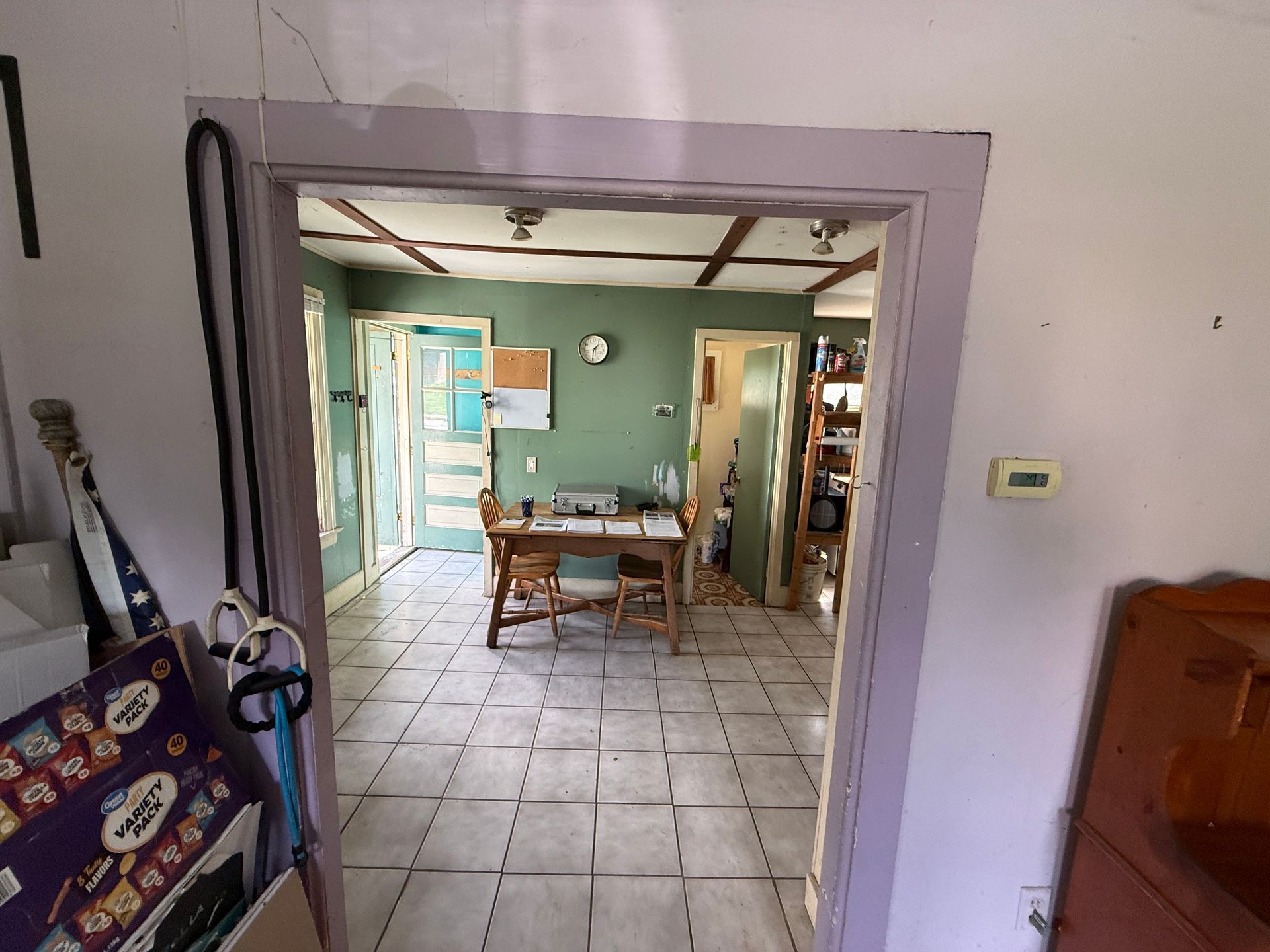 View through a doorway into a tiled dining room with a table, chairs, and green walls