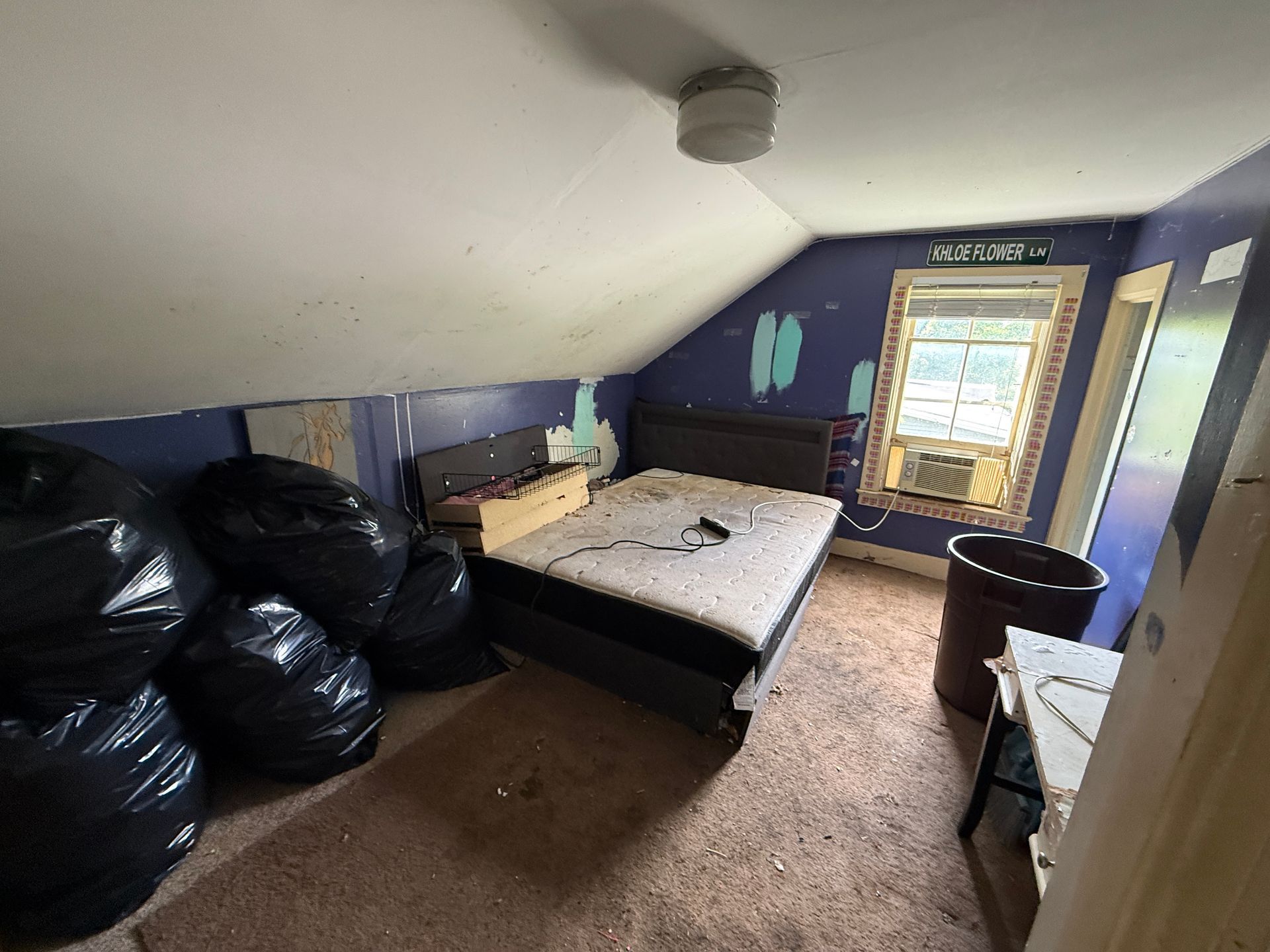 attic bedroom with bed, purple walls, and a small window.