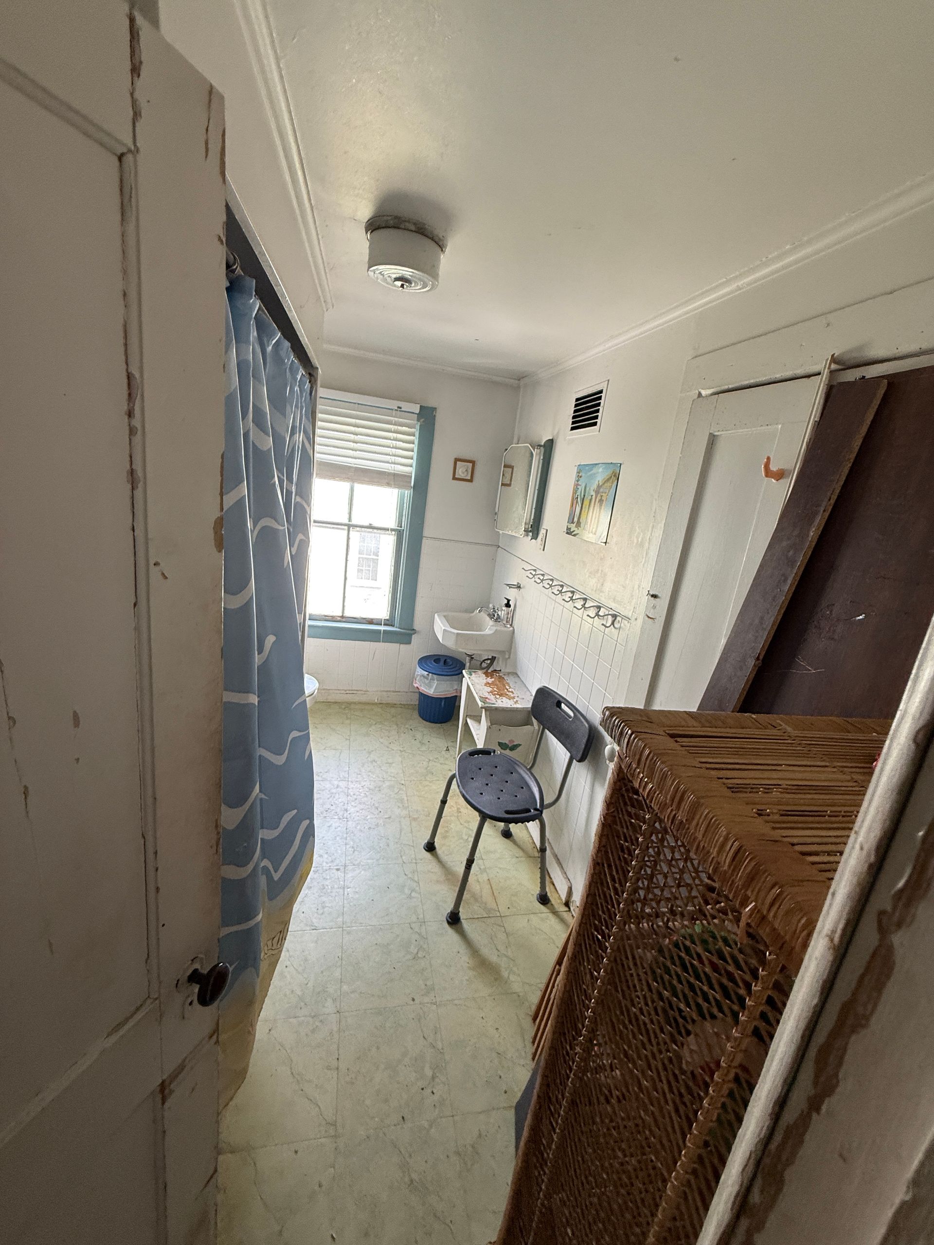 Narrow hallway with white walls, chair, small table, and bright window at the end.