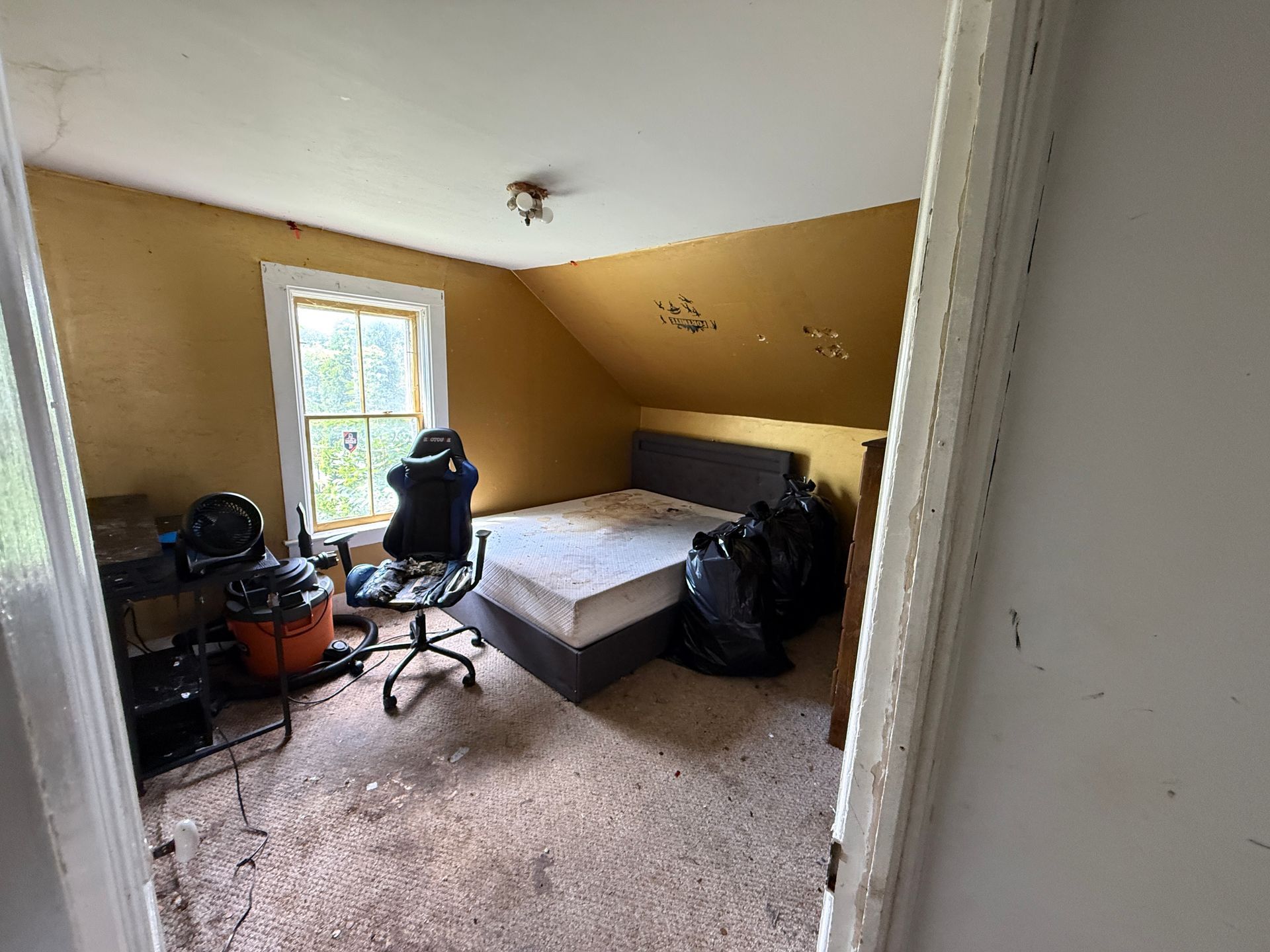 Small bedroom with a bed, desk chair, and window, viewed from the doorway.