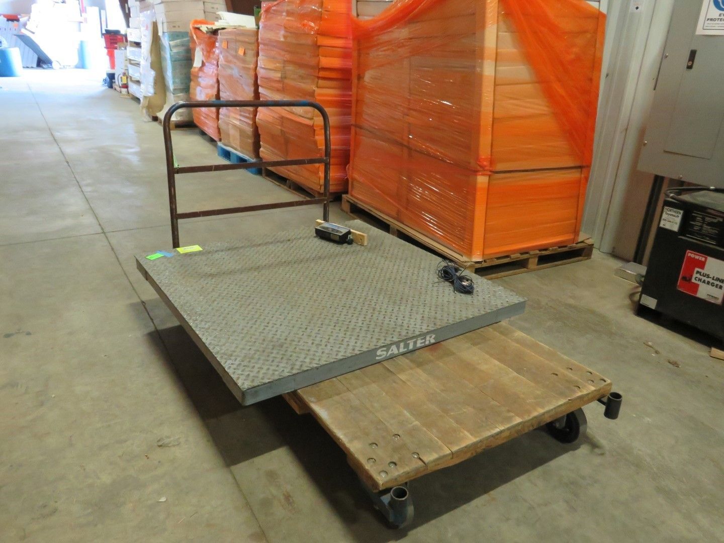 A two-tiered industrial cart in a warehouse, with a metal frame, gray top and wooden bottom.